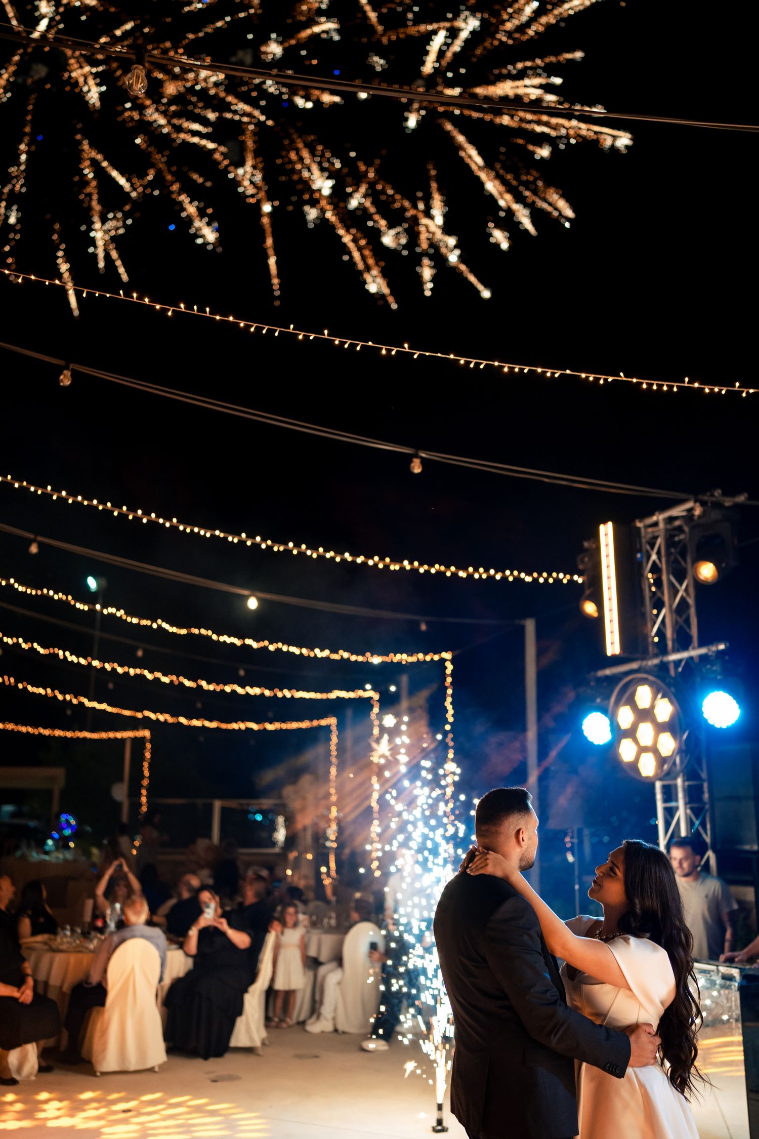 First dance at wedding reception with sparklers and string lights creating a romantic ambiance.