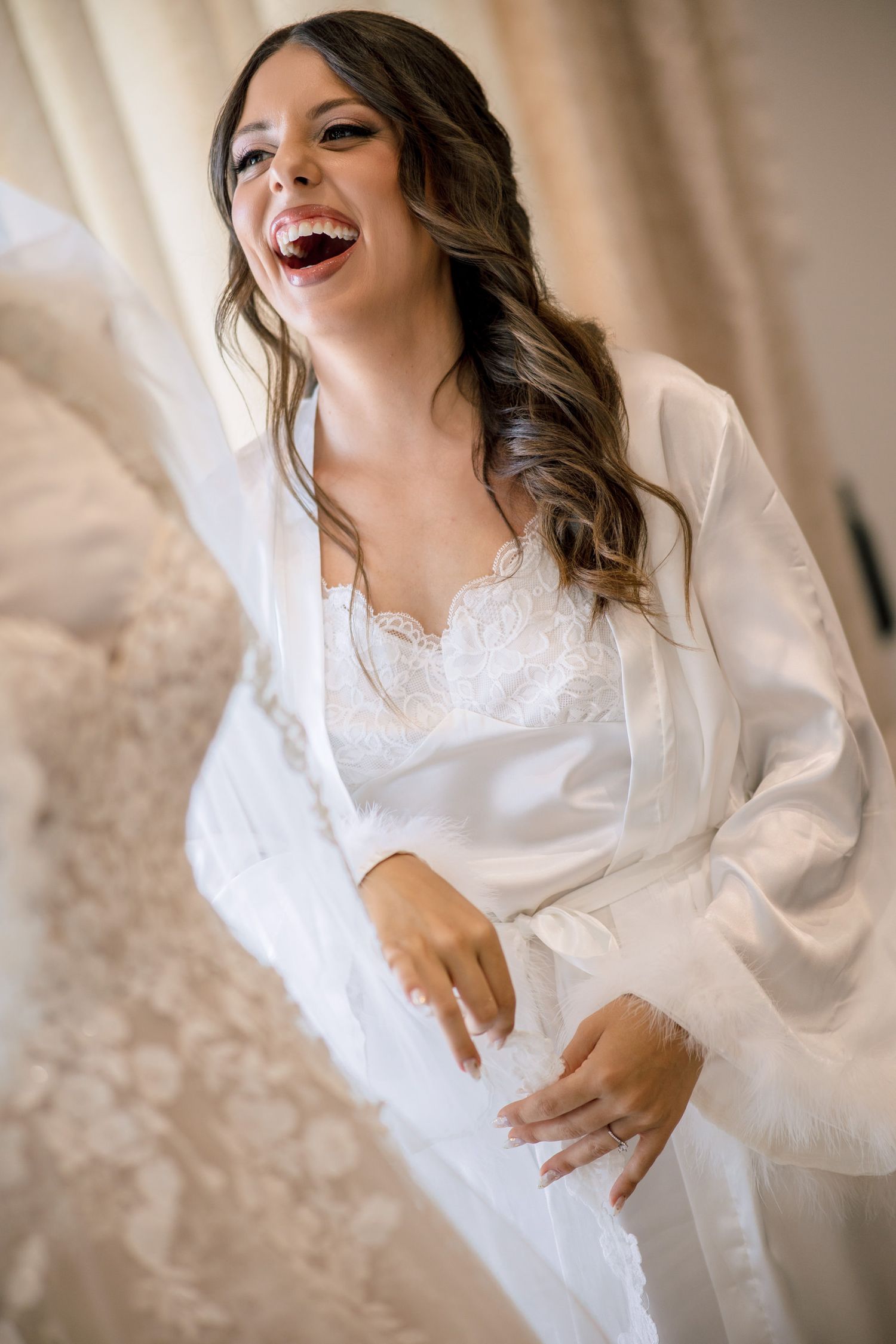 Someone in a white silk robe laughing joyfully during wedding preparations.