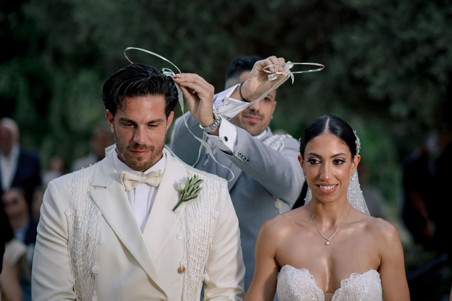 A wedding ceremony takes place outdoors with guests seated in white chairs against a scenic natural backdrop.