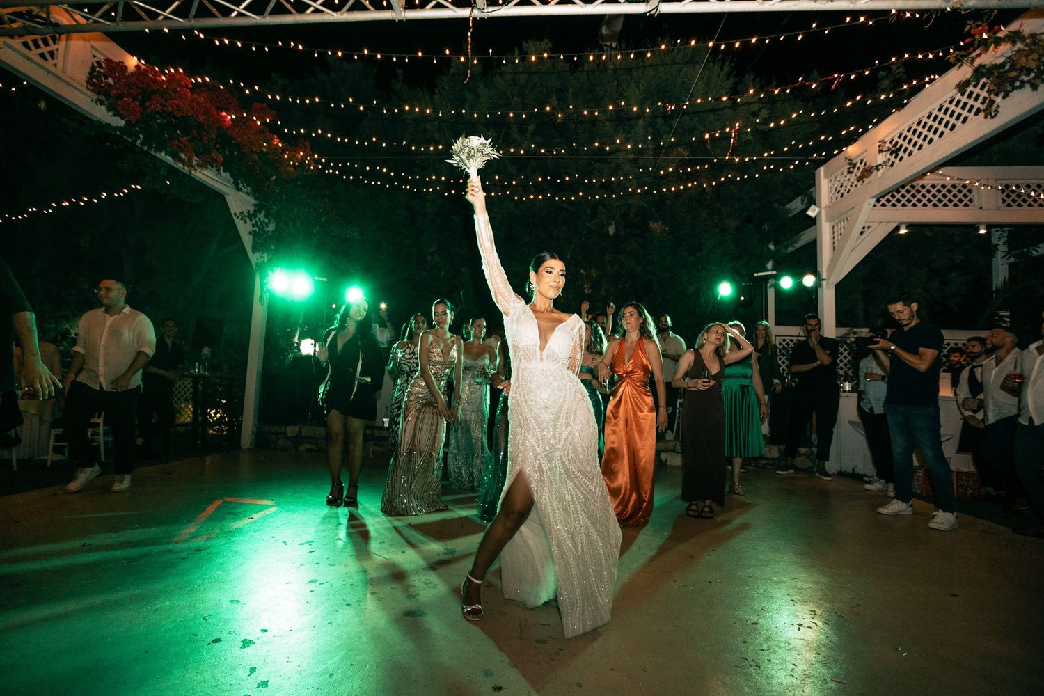Wedding celebration on an outdoor dance floor illuminated by green lights and string lighting.
