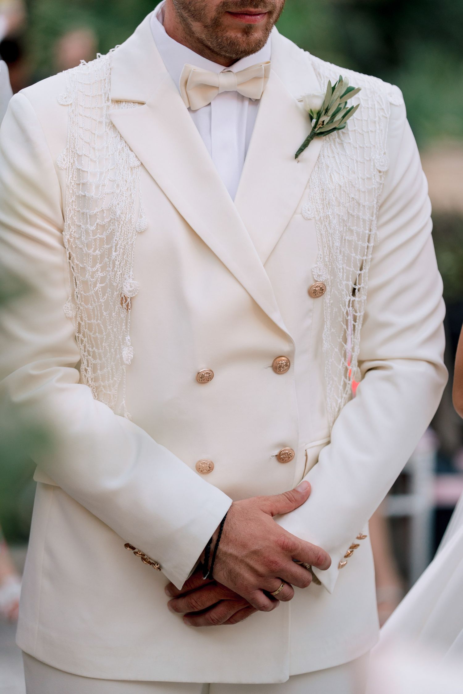 Groom wearing a detailed white double-breasted tuxedo jacket with pearl buttons.