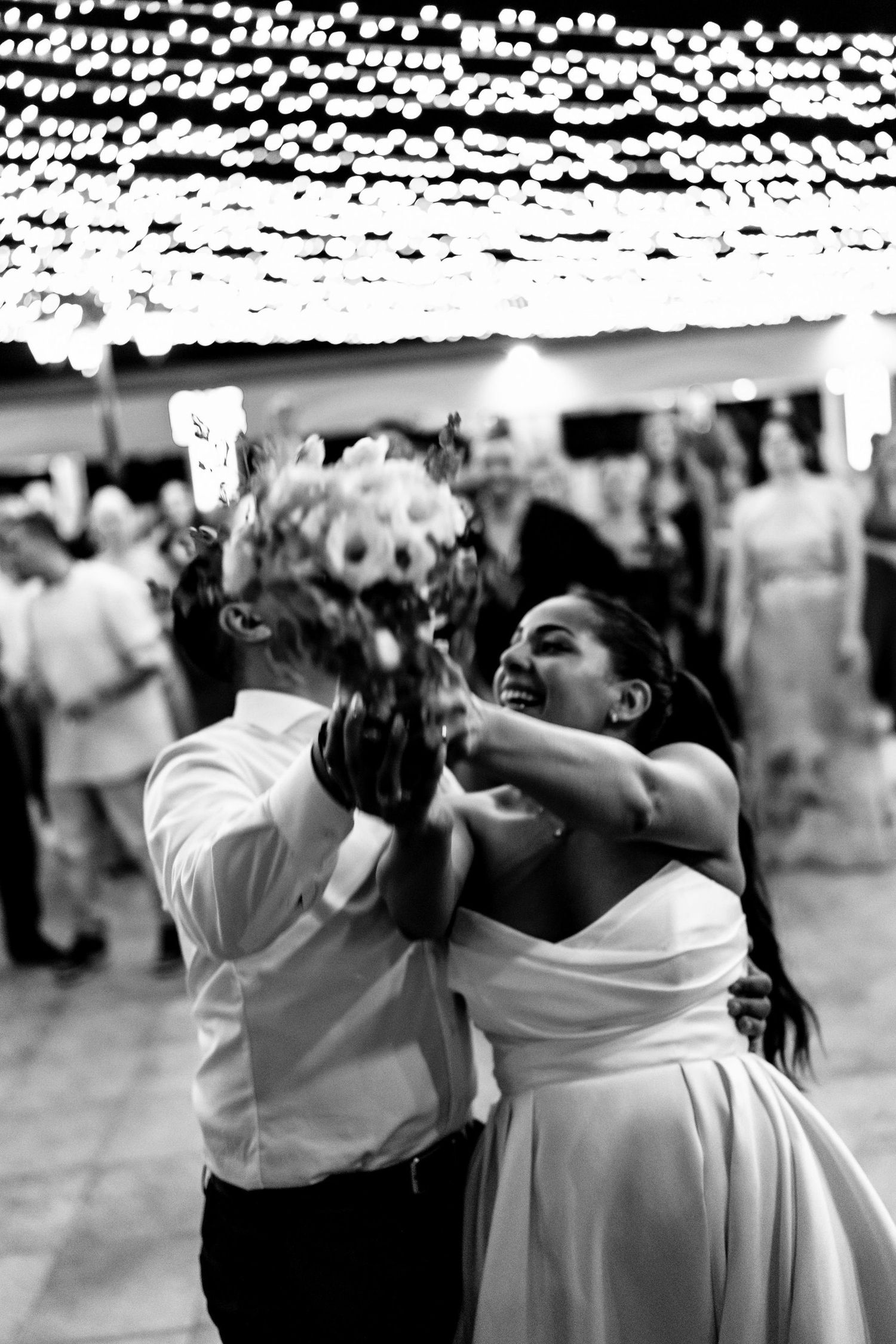 A couple dances intimately under string lights at their wedding reception.