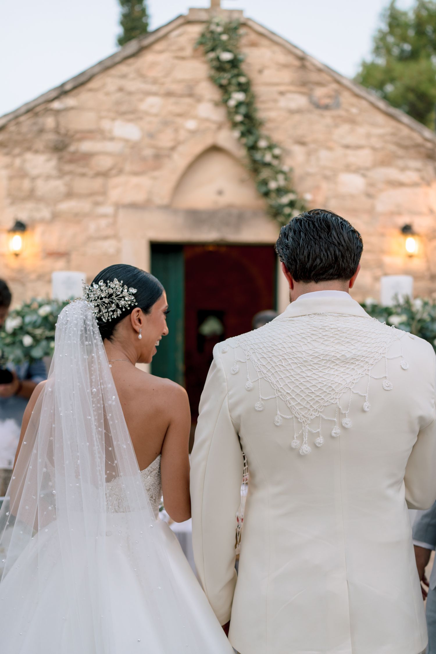 Bride and groom stand before rustic stone building with climbing vines and warm lighting.