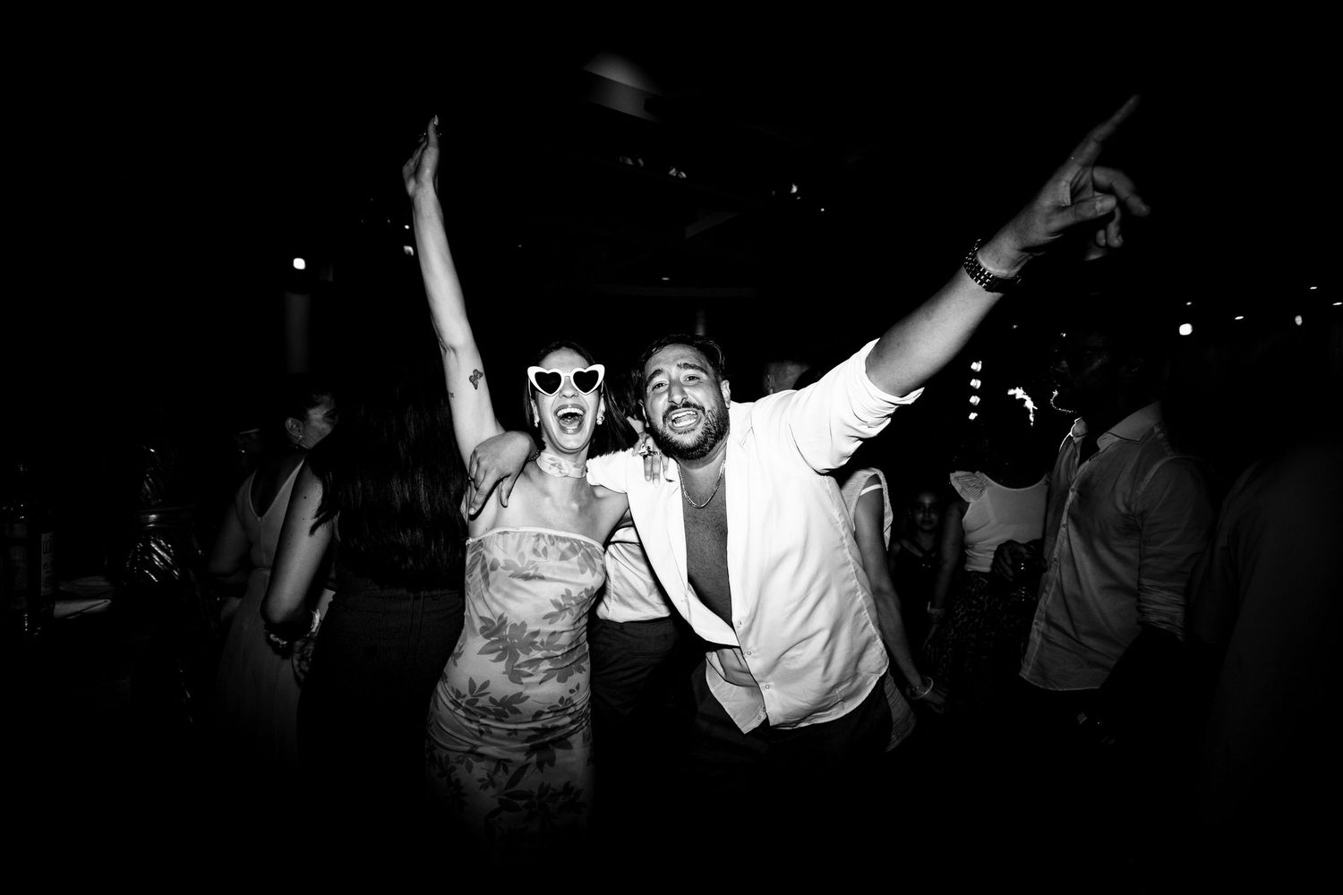 Enthusiastic party guests celebrating with arms raised in black and white photography.