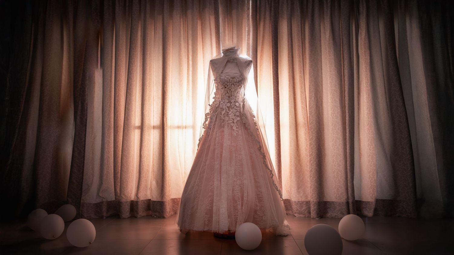 Silhouette of wedding dress against backlit curtains creating dramatic lighting effect.