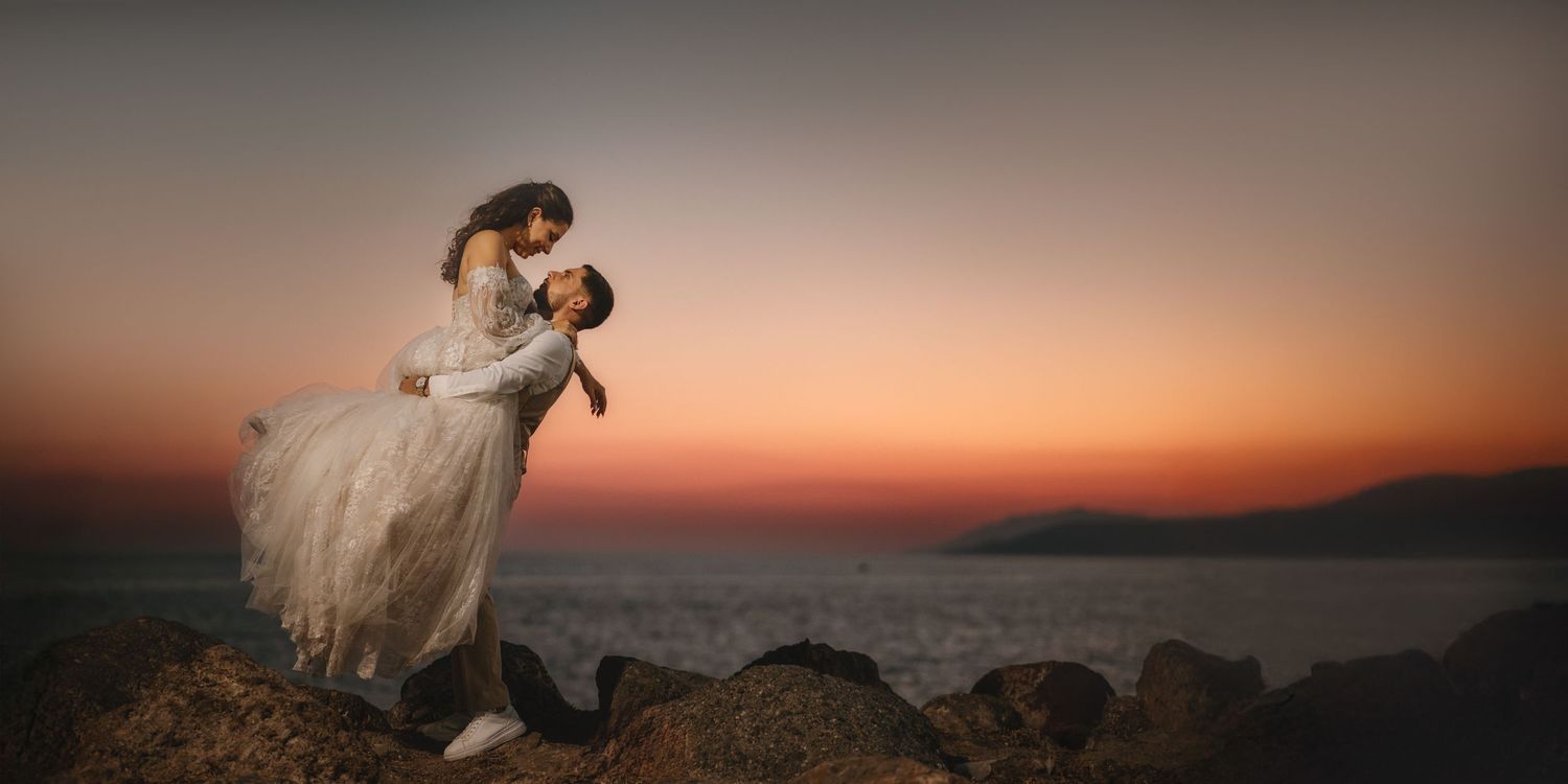 Wedding couple poses on mountain ridge during a vibrant sunset.