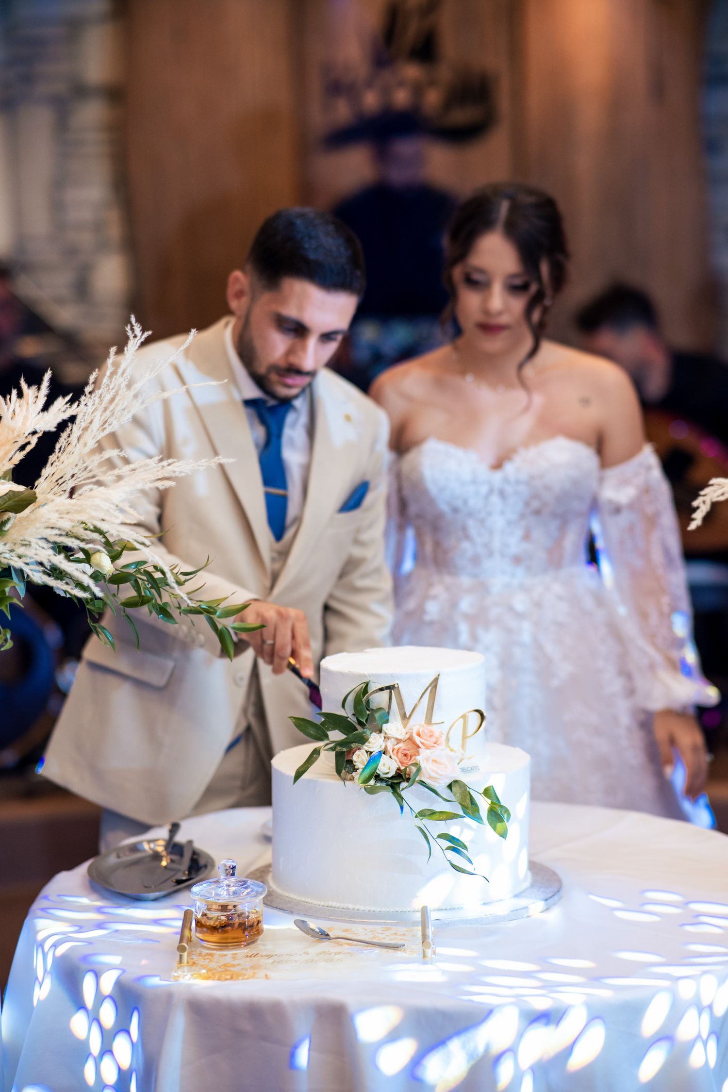 Elegant white wedding cake with floral decorations being cut on a beautifully lit table.