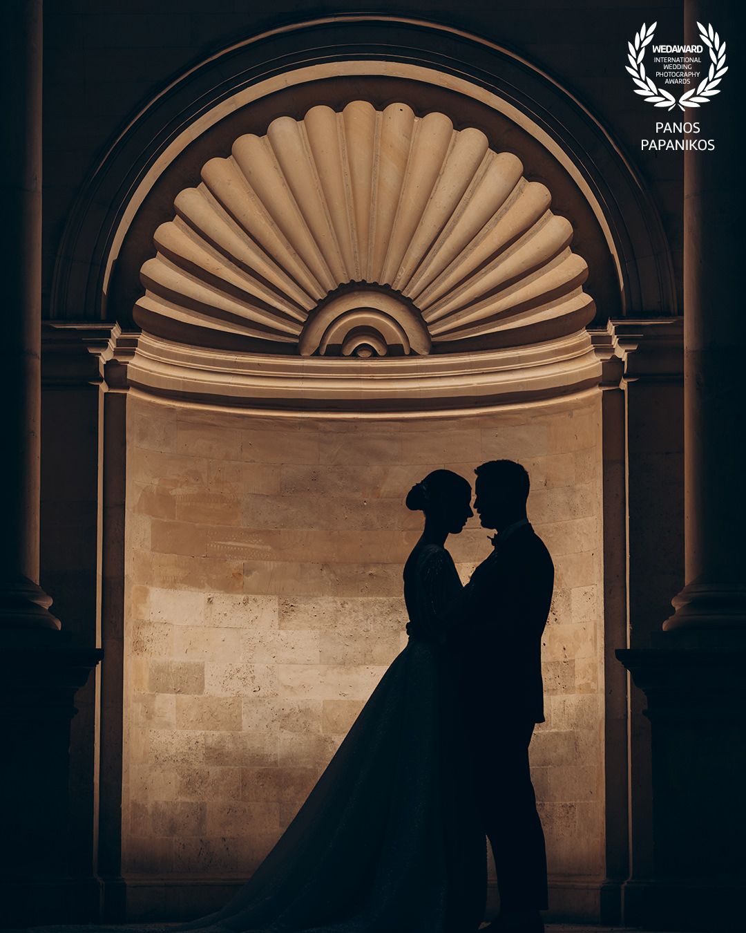 Silhouettes of a couple against dramatic archways and fan-shaped architectural details.