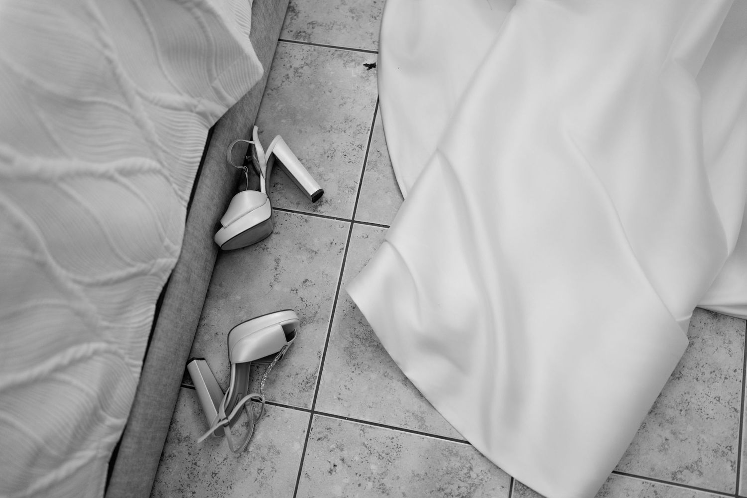 Close-up details of a white wedding dress train on tiled floor.