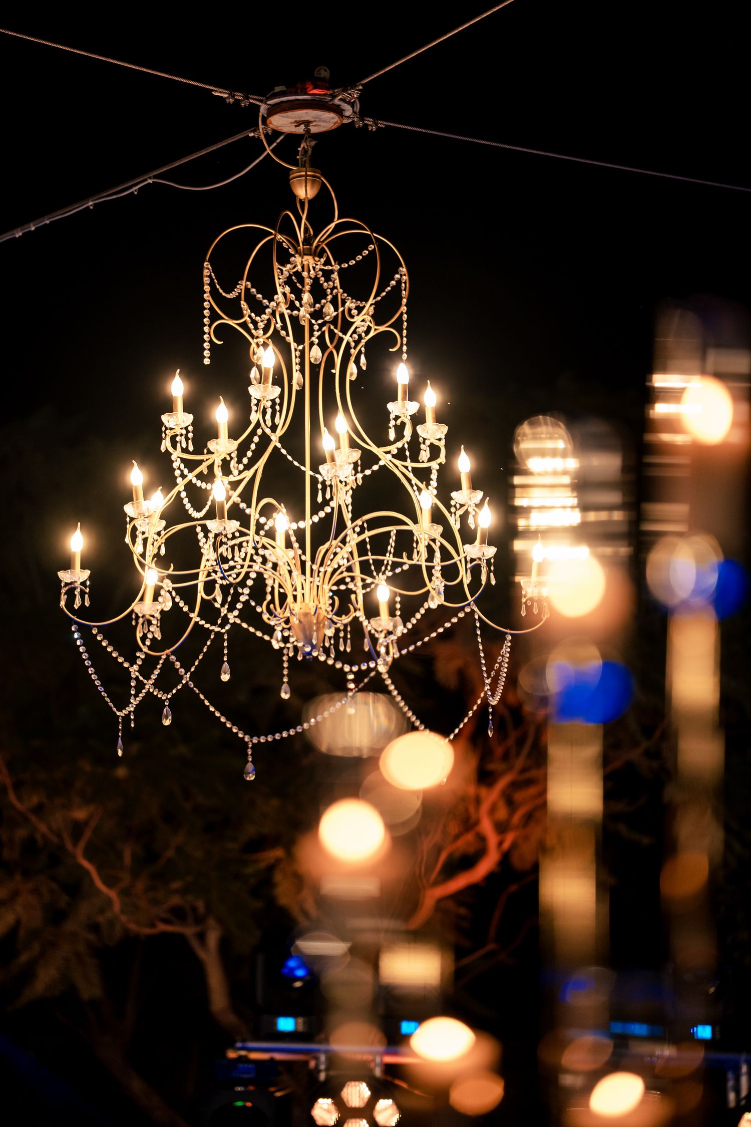 Elegant crystal chandeliers hang outdoors creating romantic wedding reception lighting.