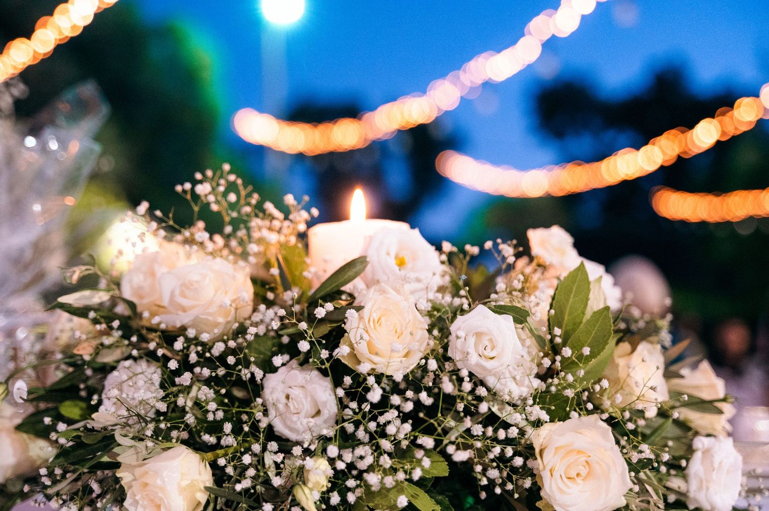 White floral arrangements with baby's breath under twinkling string lights at dusk.