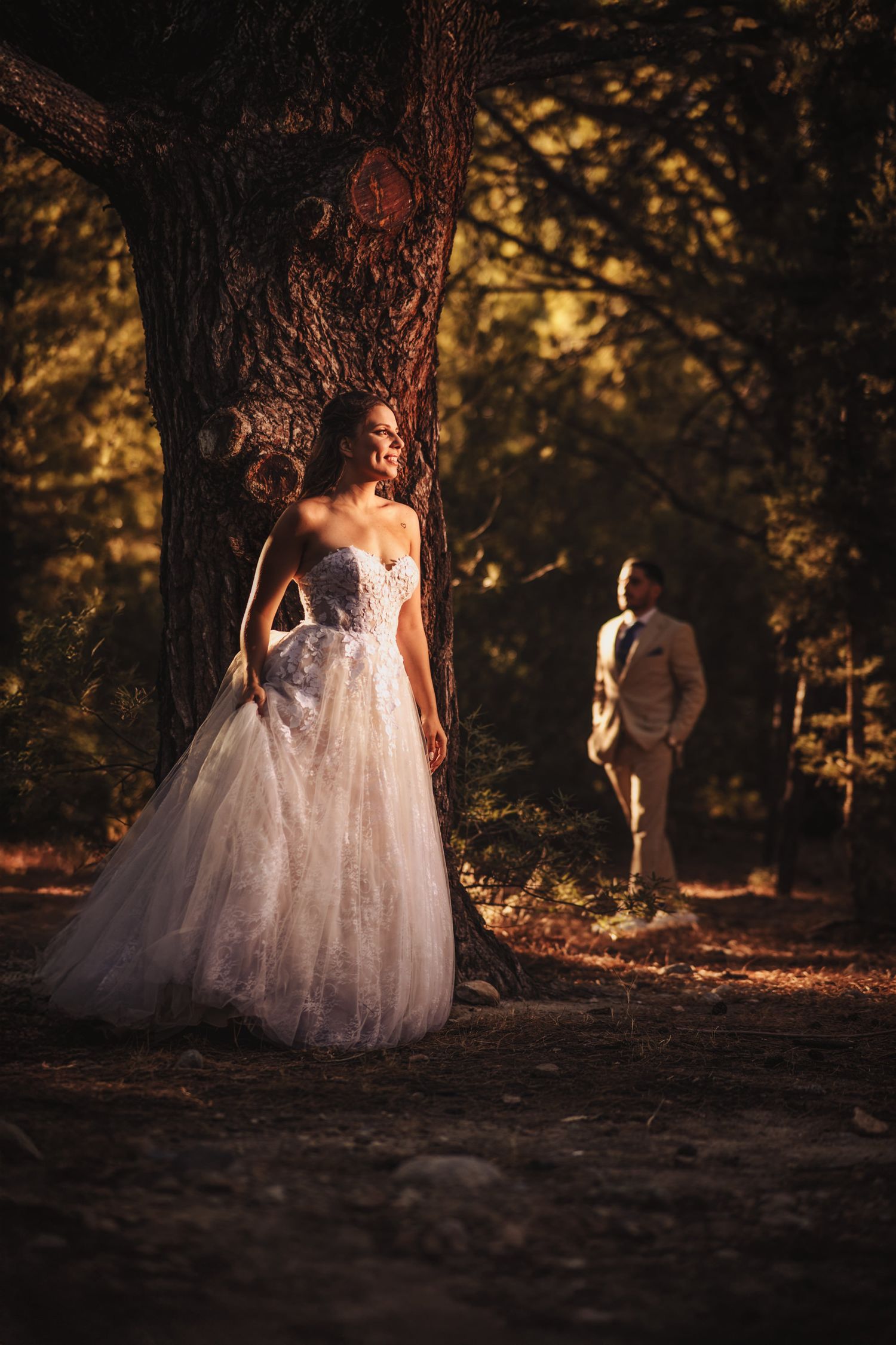 Elegant white wedding dress contrasts against dark forest floor in dappled sunlight.