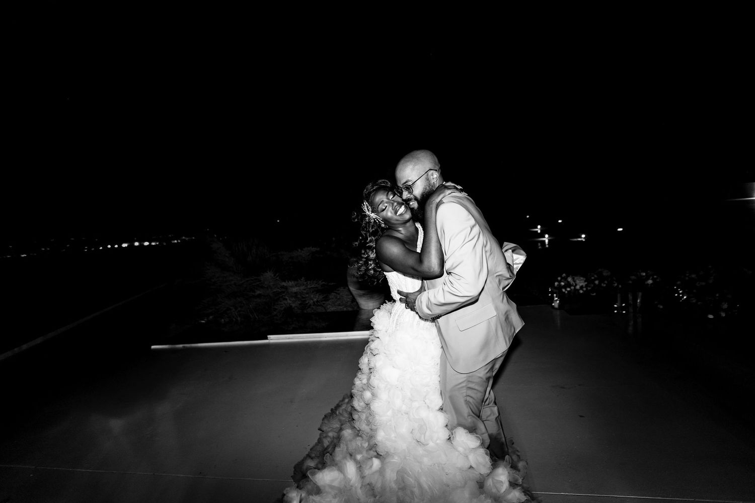 A black and white wedding photo capturing an intimate dance moment under the night sky.