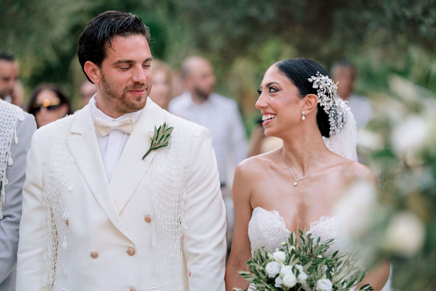 Wedding couple in all-white attire poses together in an outdoor garden setting.