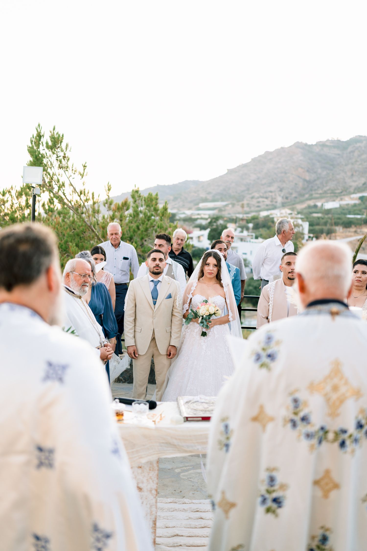 Wedding party members in light colored attire stand together during outdoor ceremony.