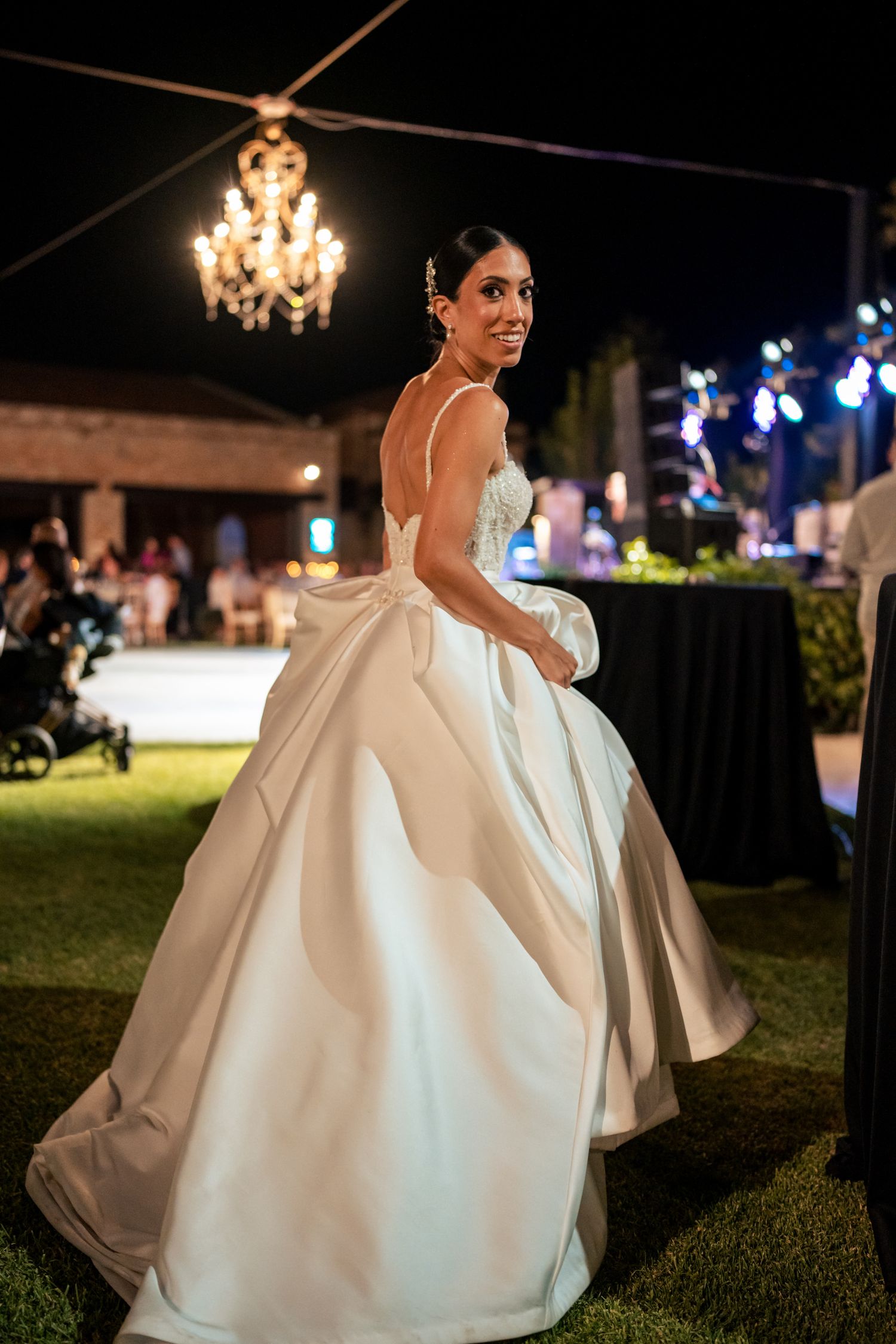 Elegant wedding gown photographed under a chandelier during an outdoor evening reception.
