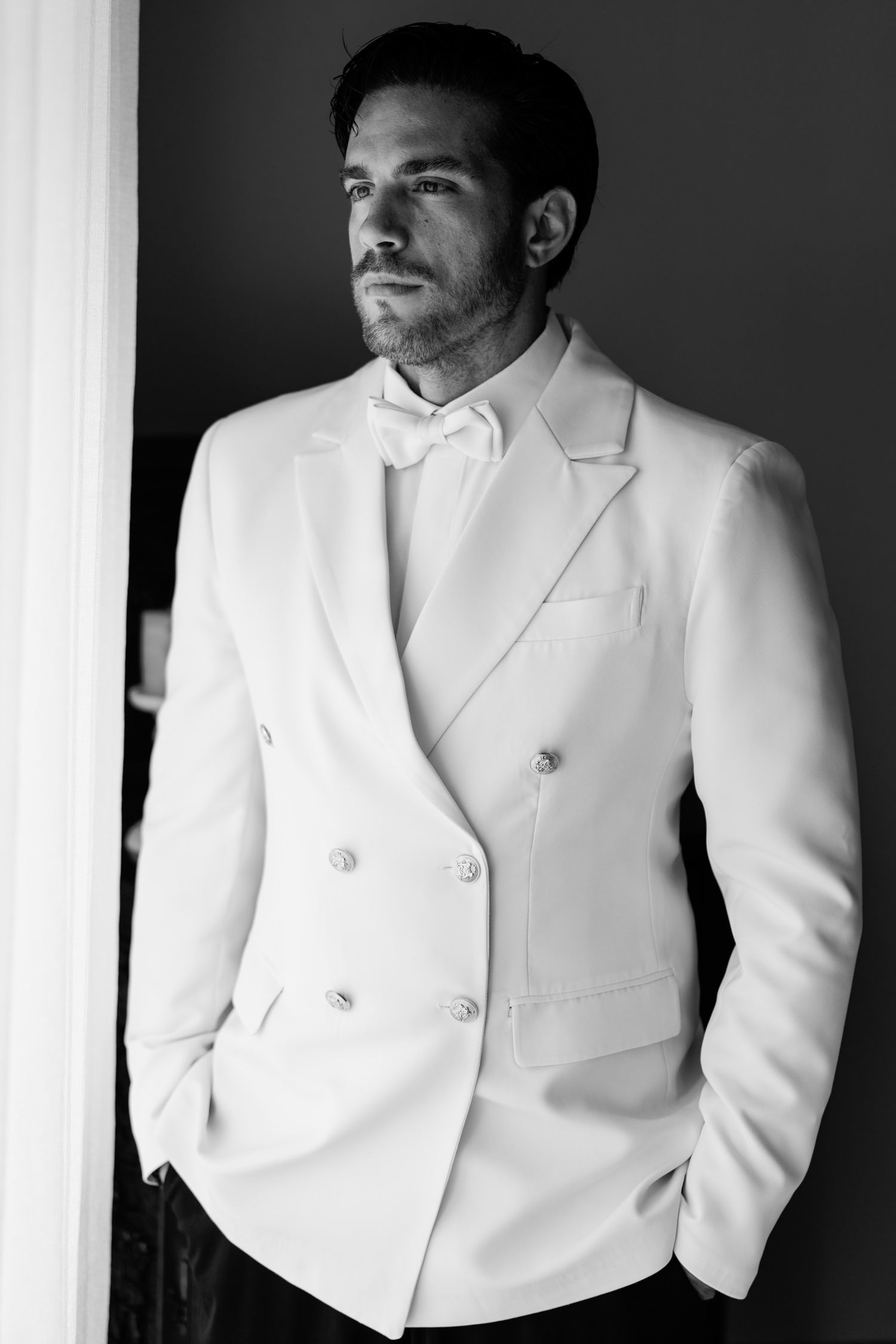 Classic black and white portrait of a groom wearing a crisp white double-breasted tuxedo jacket.