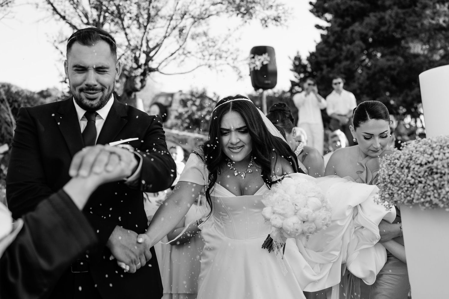 Wedding celebration with guests throwing confetti outdoors.
