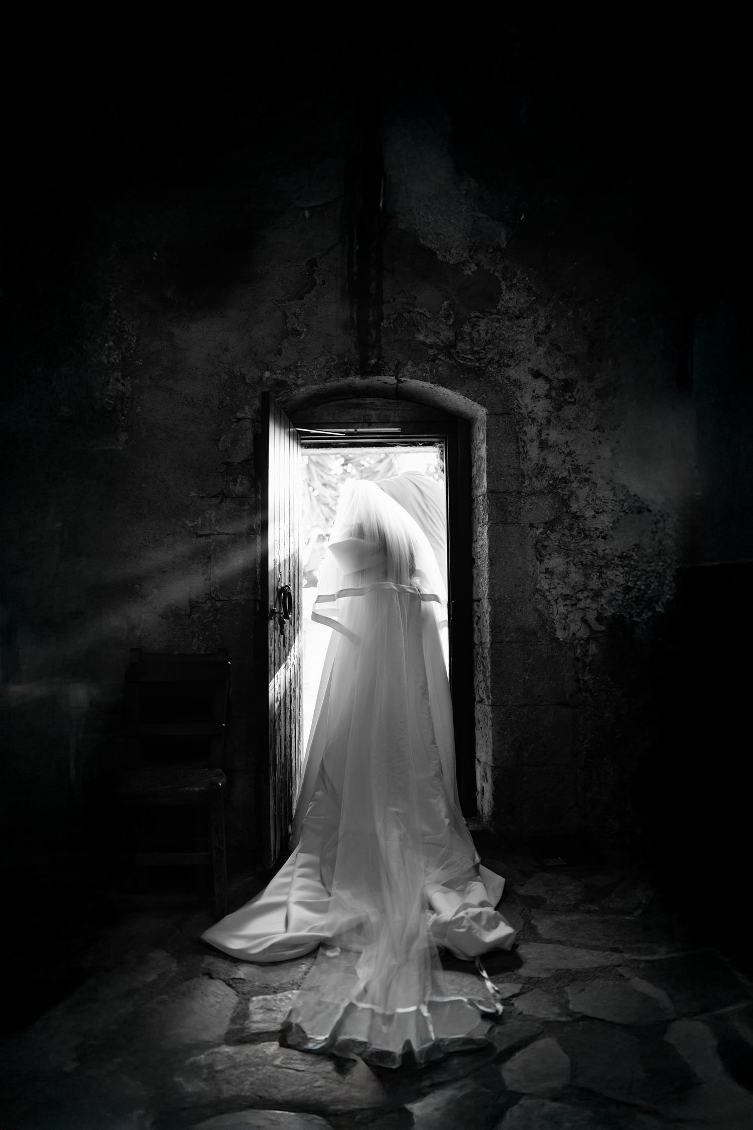 Wedding dress displayed dramatically in doorway with moody lighting.