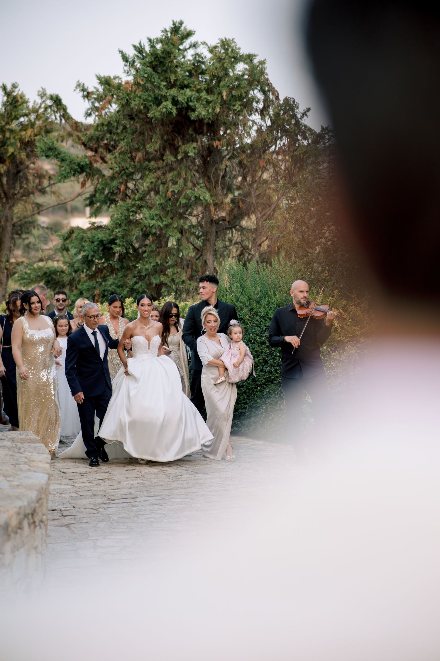 Wedding party walking along stone pathway framed through natural foliage.