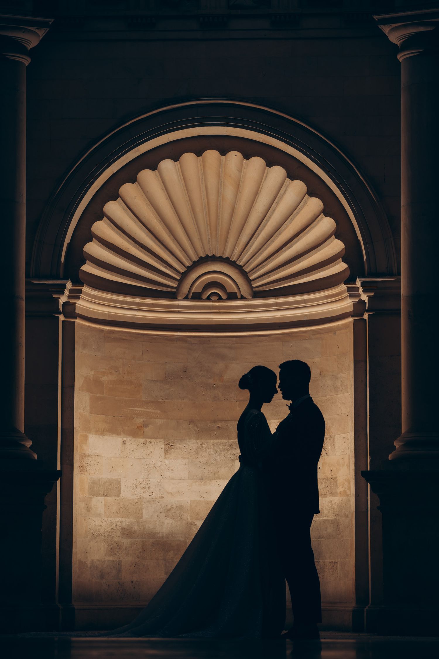 Silhouetted couple against architectural arches with dramatic backlighting.