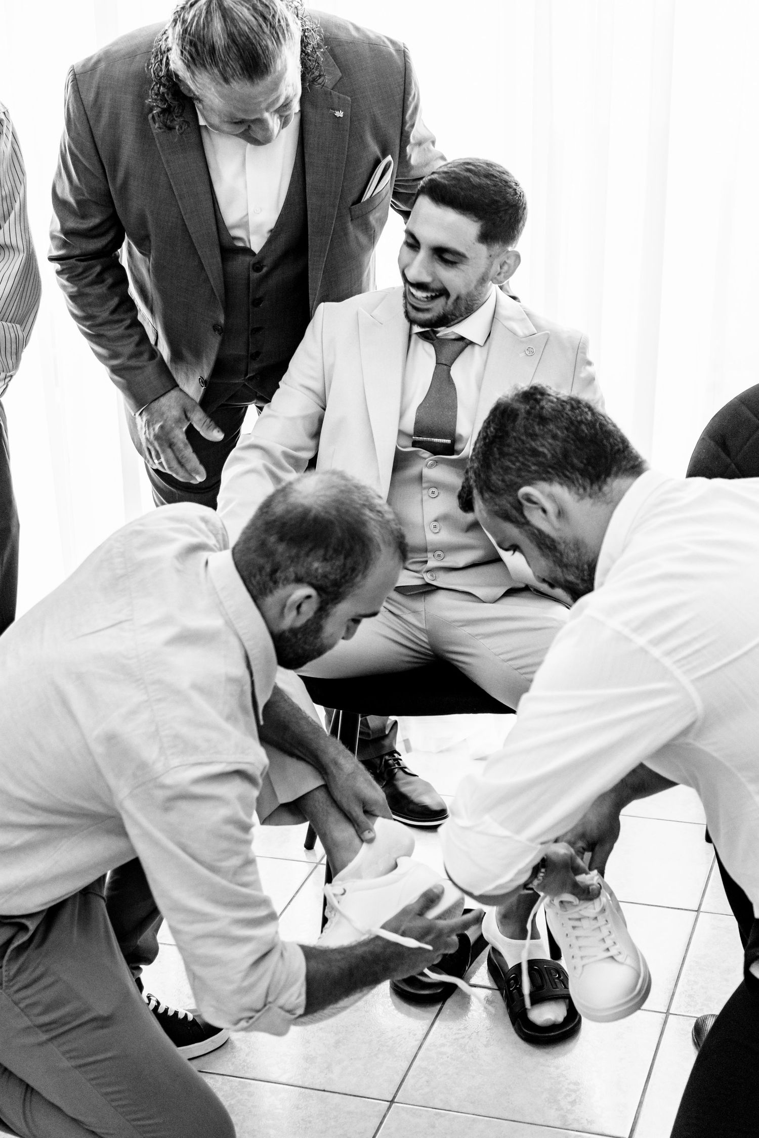 Groomsmen help adjust shoes and clothing details before wedding ceremony.