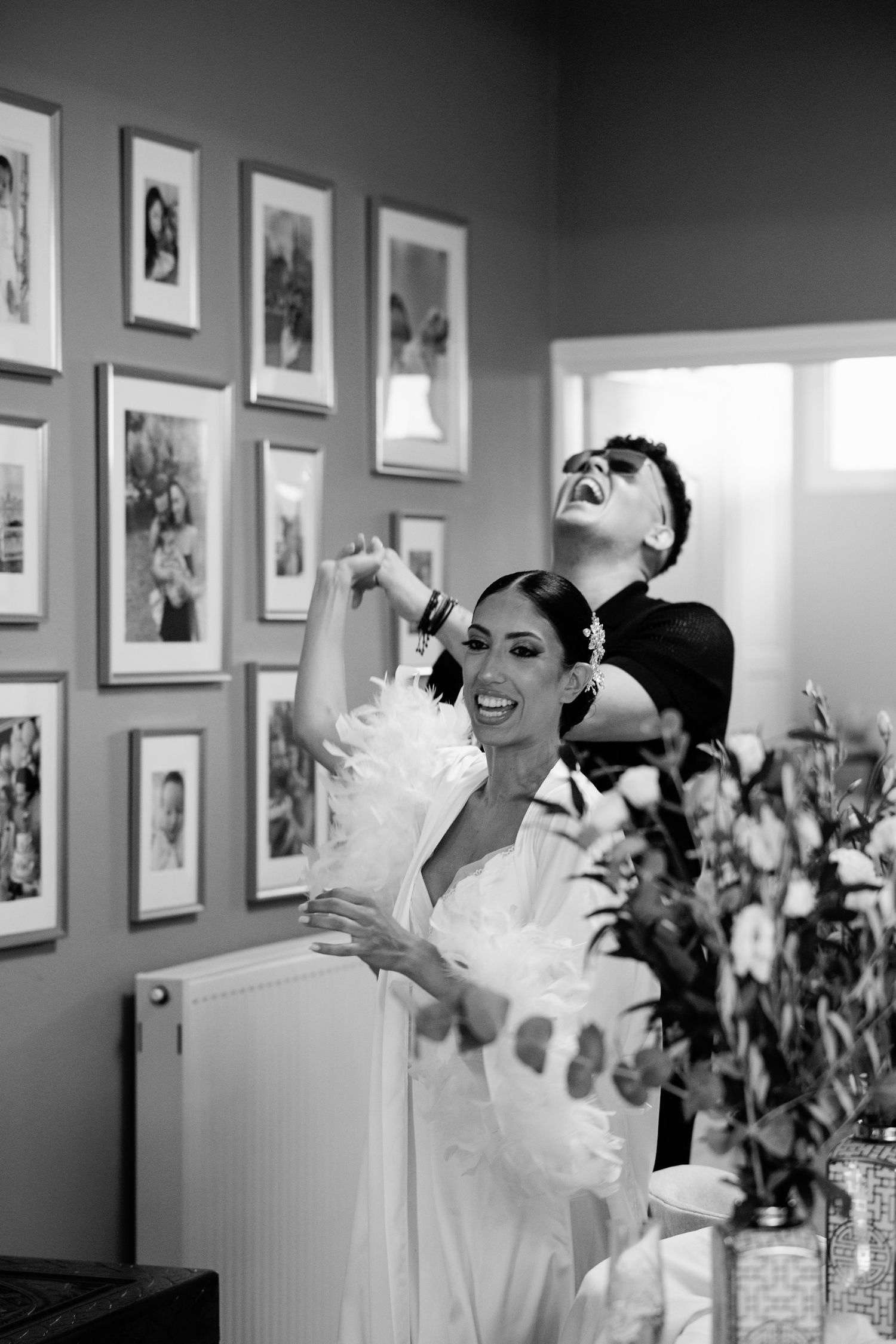 Wedding party members celebrate in a room with framed photos on the wall.