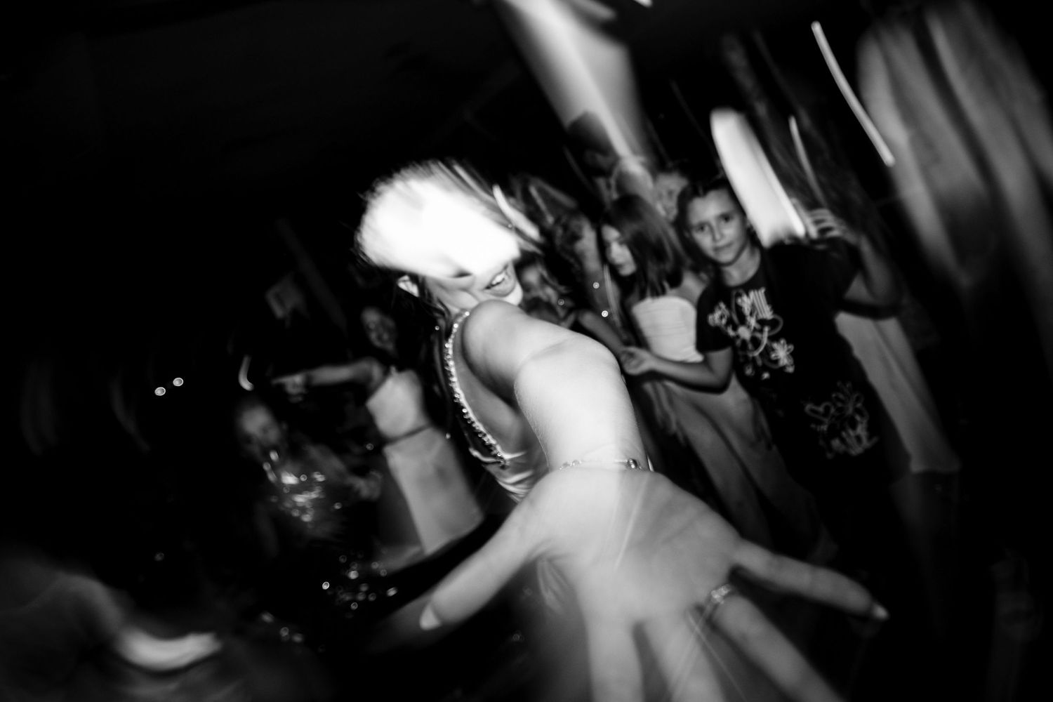 Motion-blurred black and white photo of party guests dancing at a celebration.