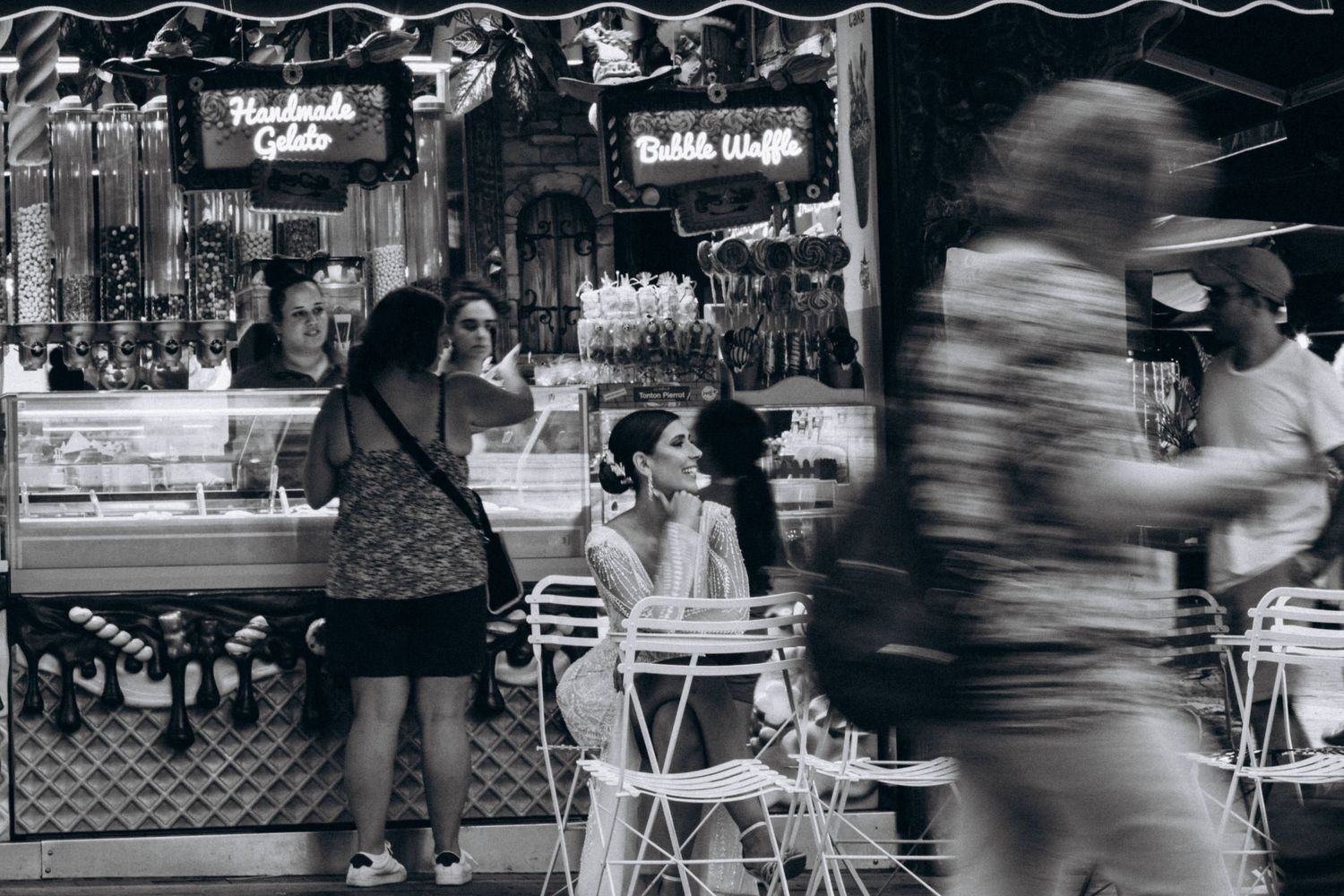 Black and white street scene with motion blur at outdoor cafe seating area.