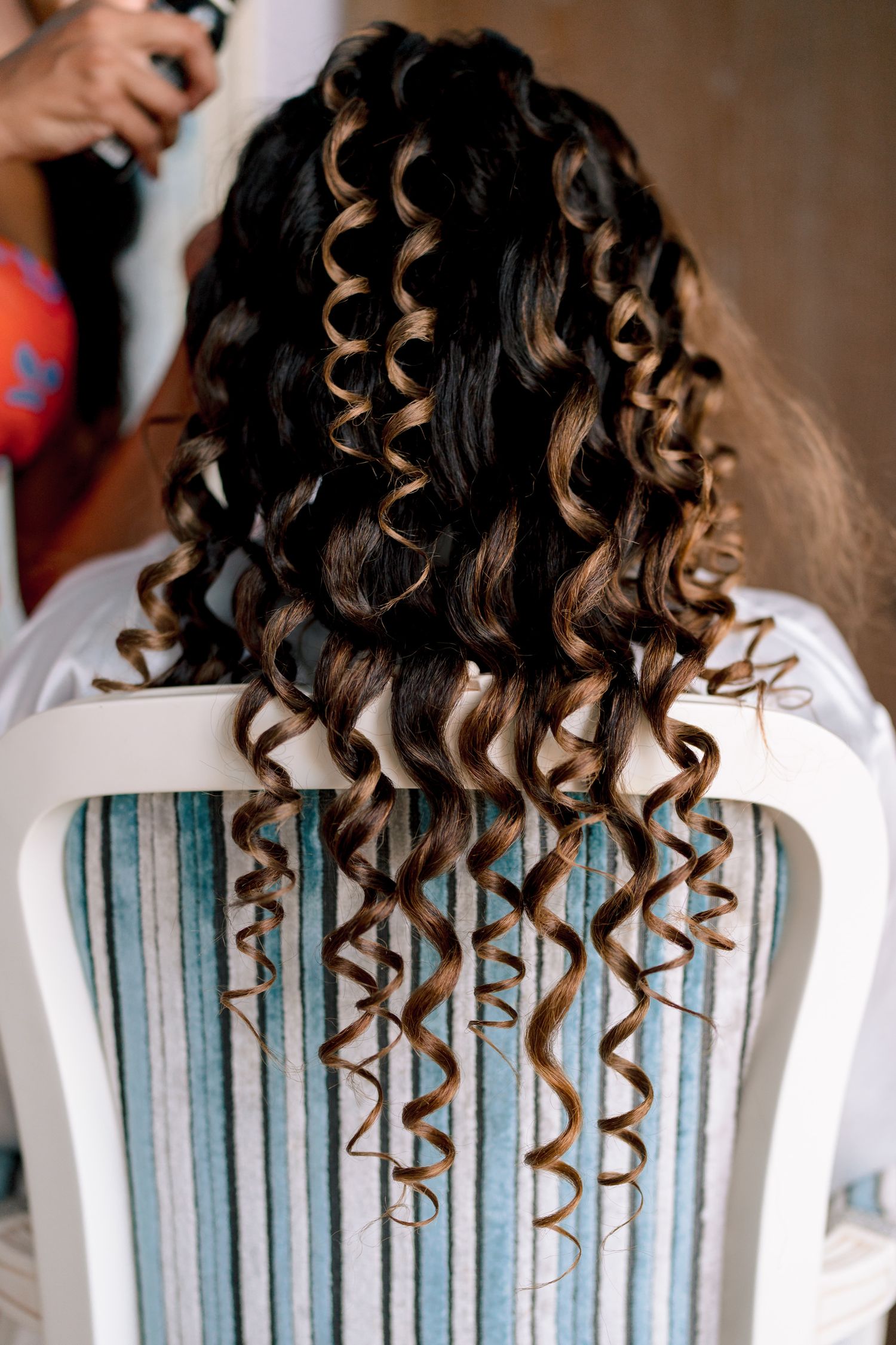 Back view of perfectly styled spiral curls in dark hair with caramel highlights.