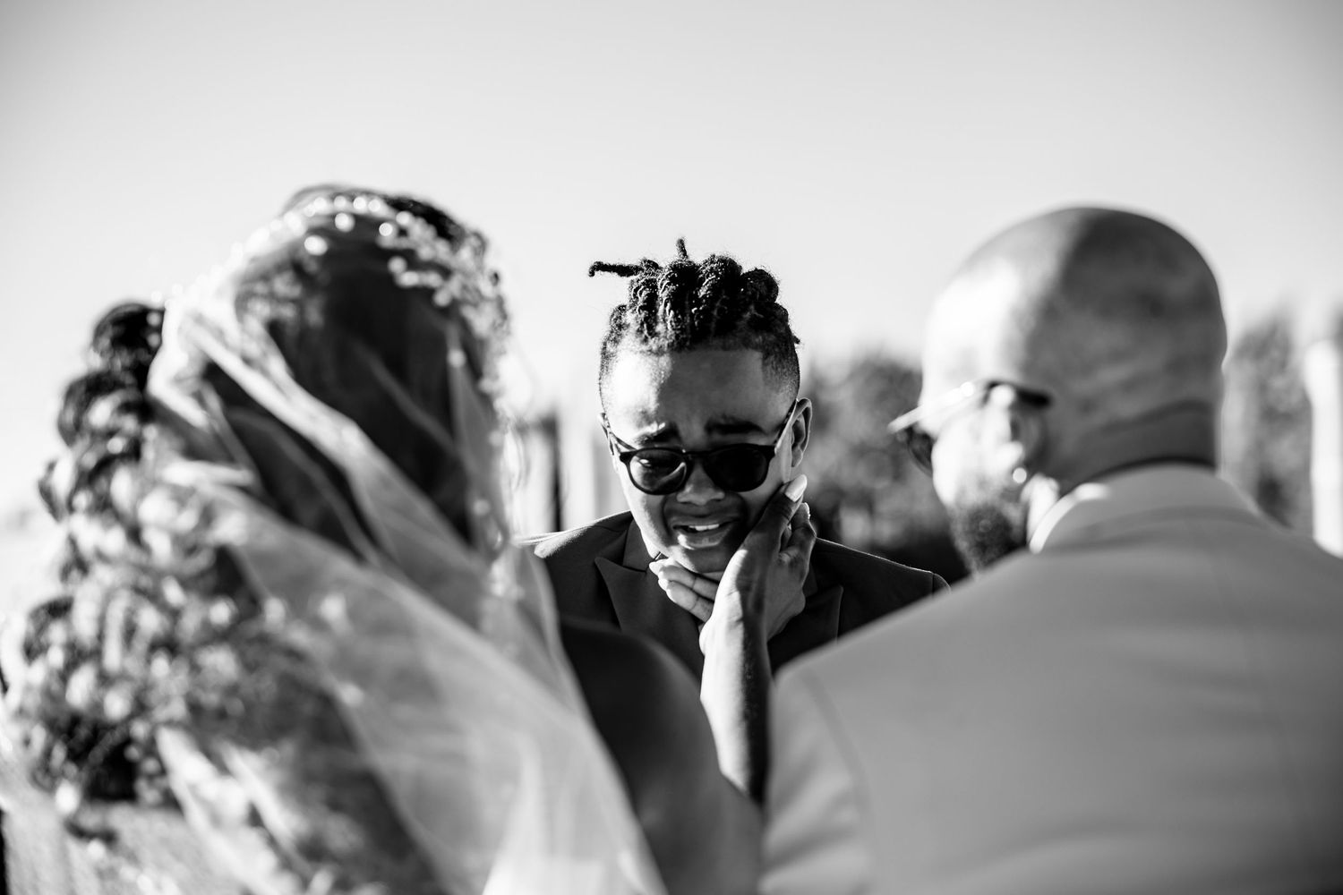 Wedding guests in formal attire gathered outdoors on a sunny day.