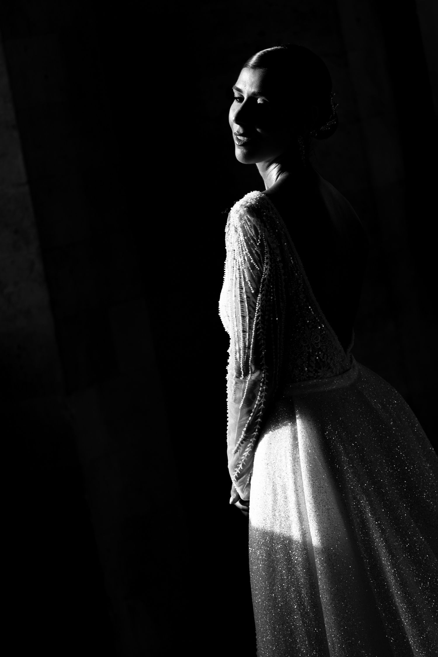 Artistic black and white portrait of a bride in a beaded gown with dramatic side lighting.