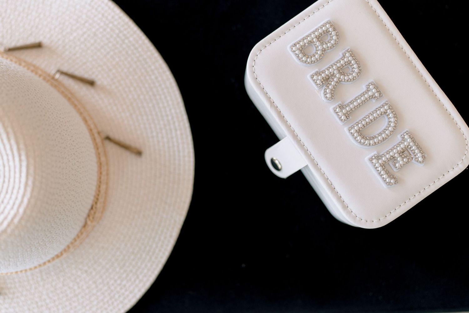 White sun hat and bride accessory bag arranged on black background.