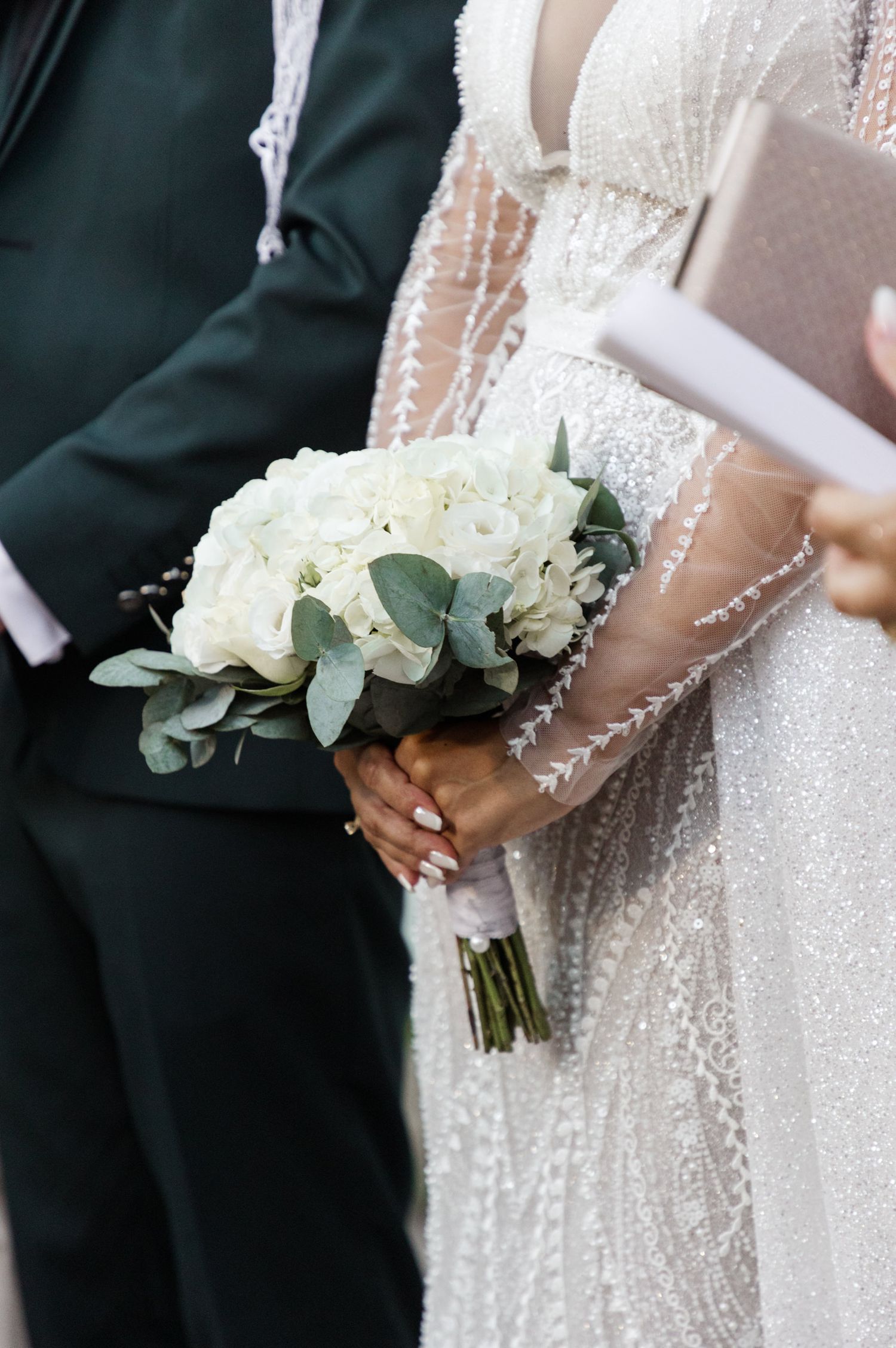 Classic white rose and eucalyptus wedding bouquet held against a beaded wedding dress.