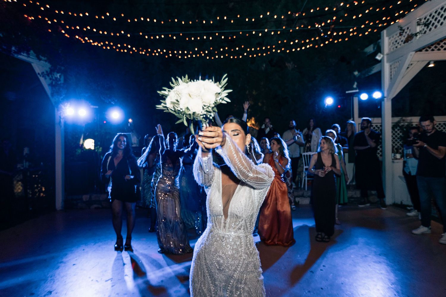 Outdoor nighttime celebration with blue lighting and string light decorations overhead.