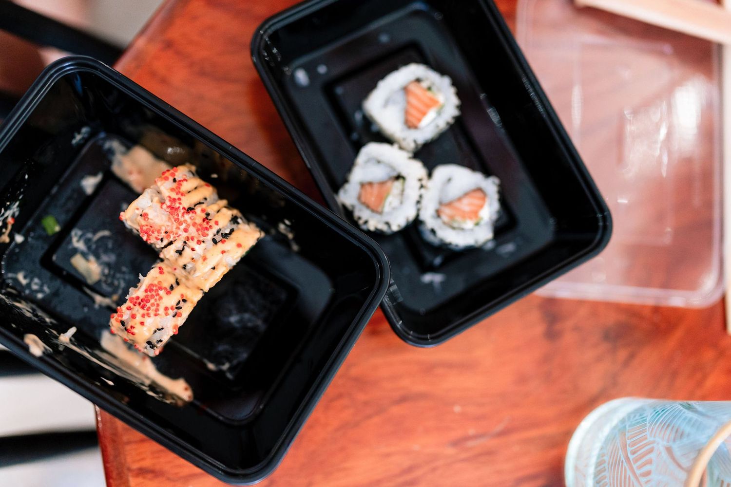 Various sushi rolls and Japanese dishes arranged in black takeout containers.