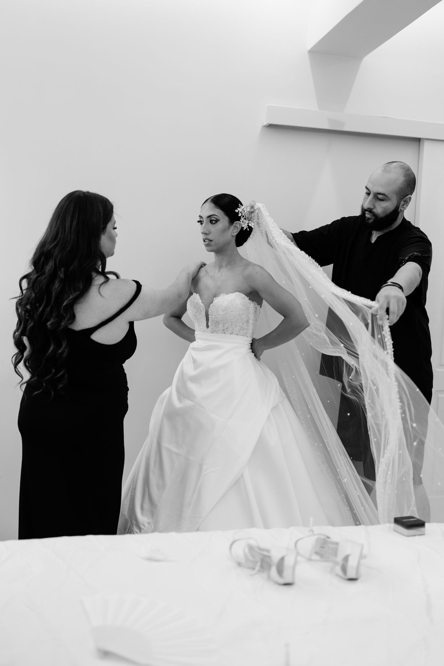 Black and white photo shows wedding dress preparations with attendants helping.