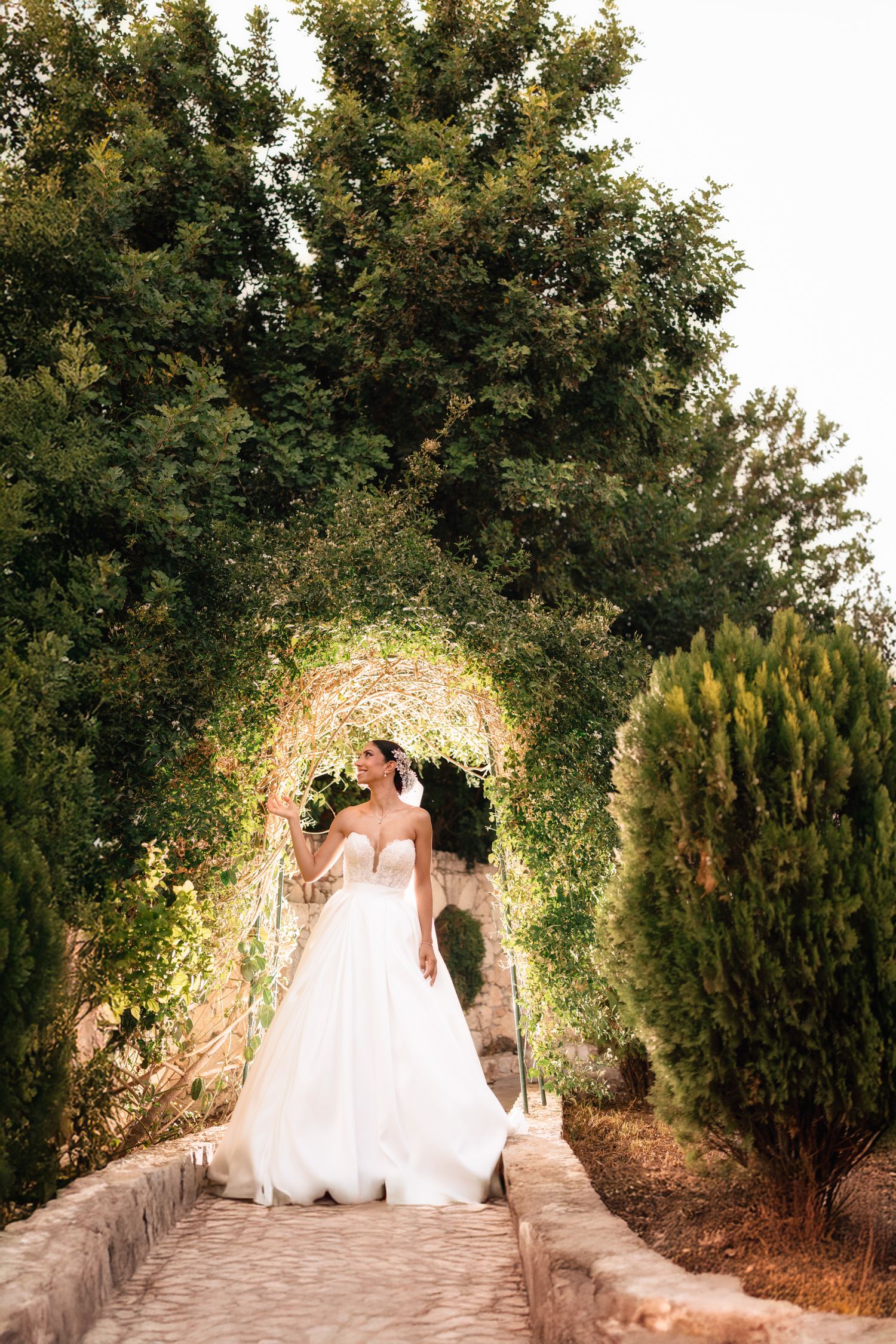 A bride in a white gown walking through a floral garden arch.