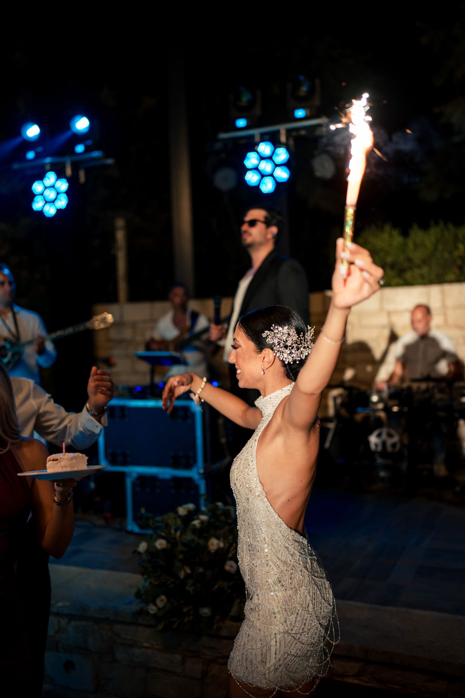 Bride holding sparkler while dancing at nighttime wedding reception with band performing.