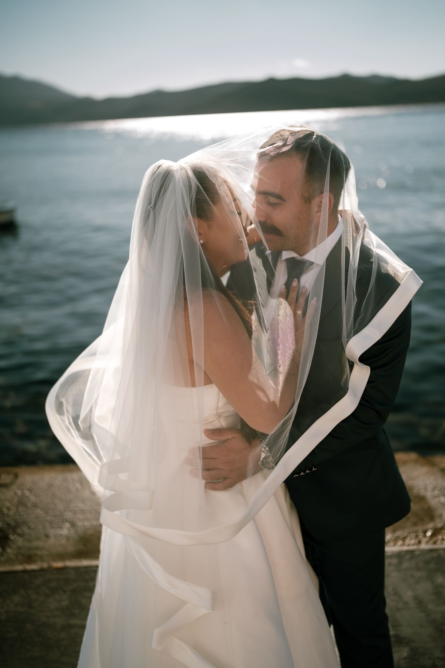 A couple shares intimate moments by a lake with mountains in the background.