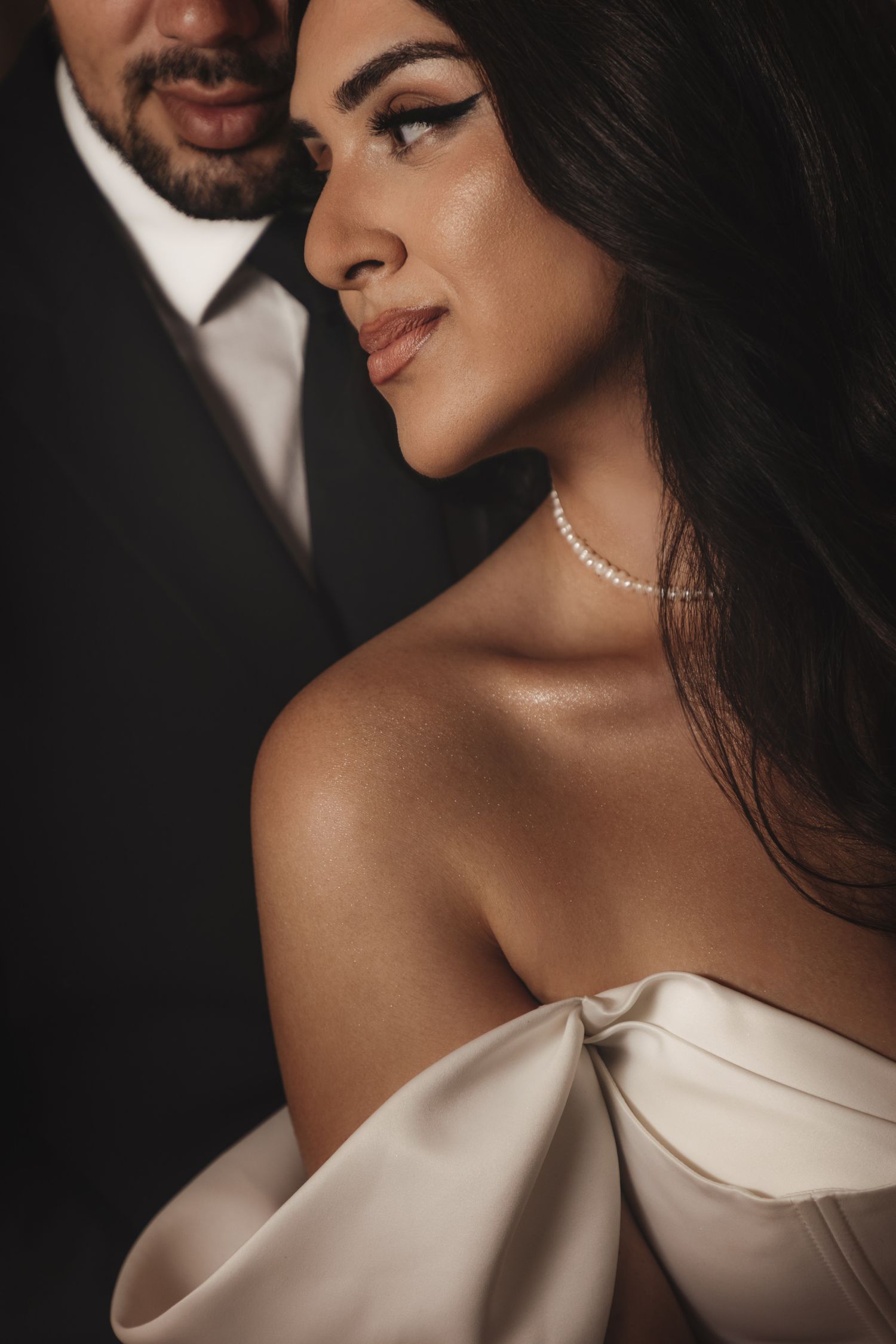 Close-up portrait showcasing elegant bridal details including pearl necklace and off-shoulder gown.