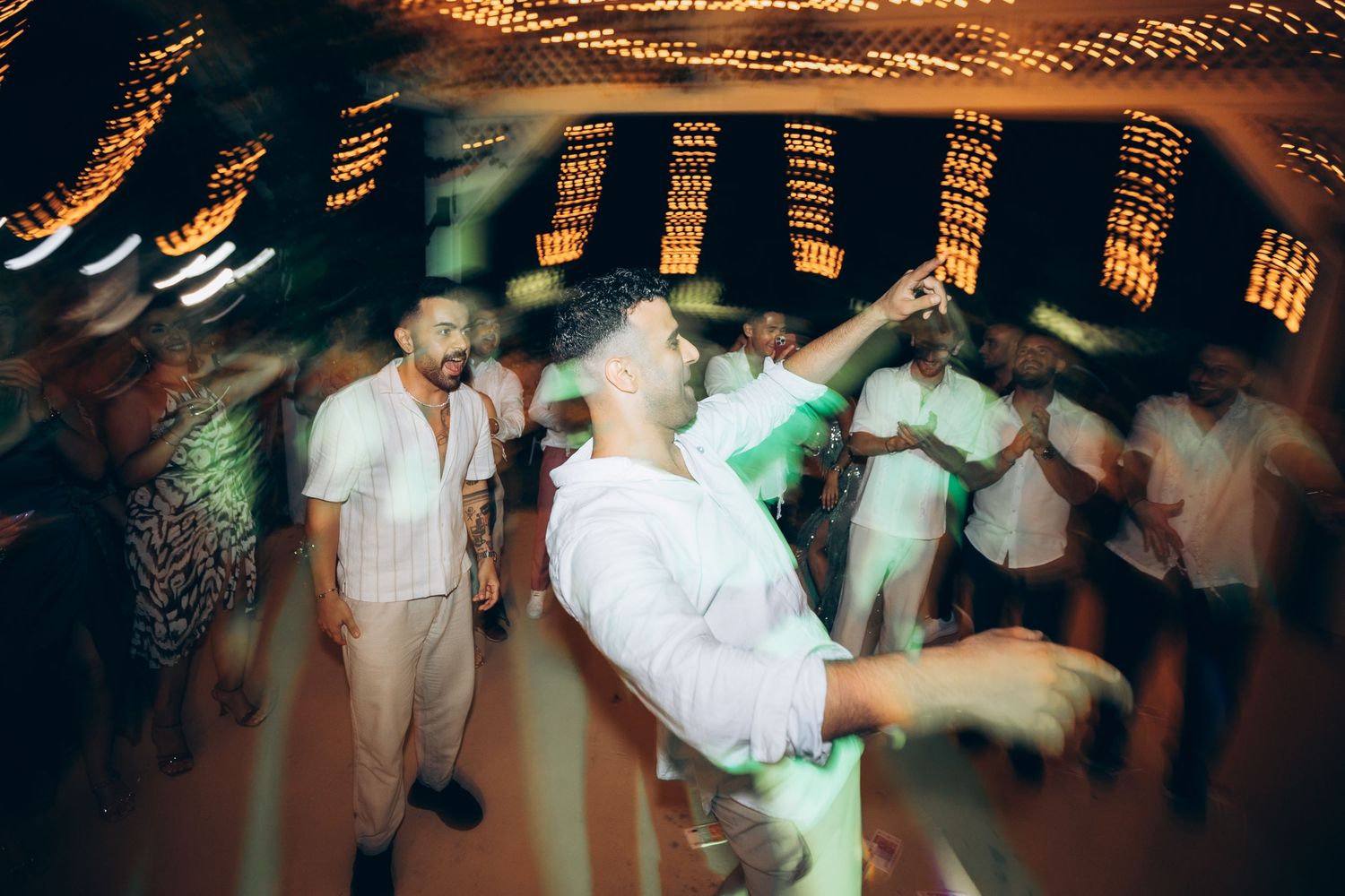 Wedding reception dance floor filled with guests under ambient string light decorations.