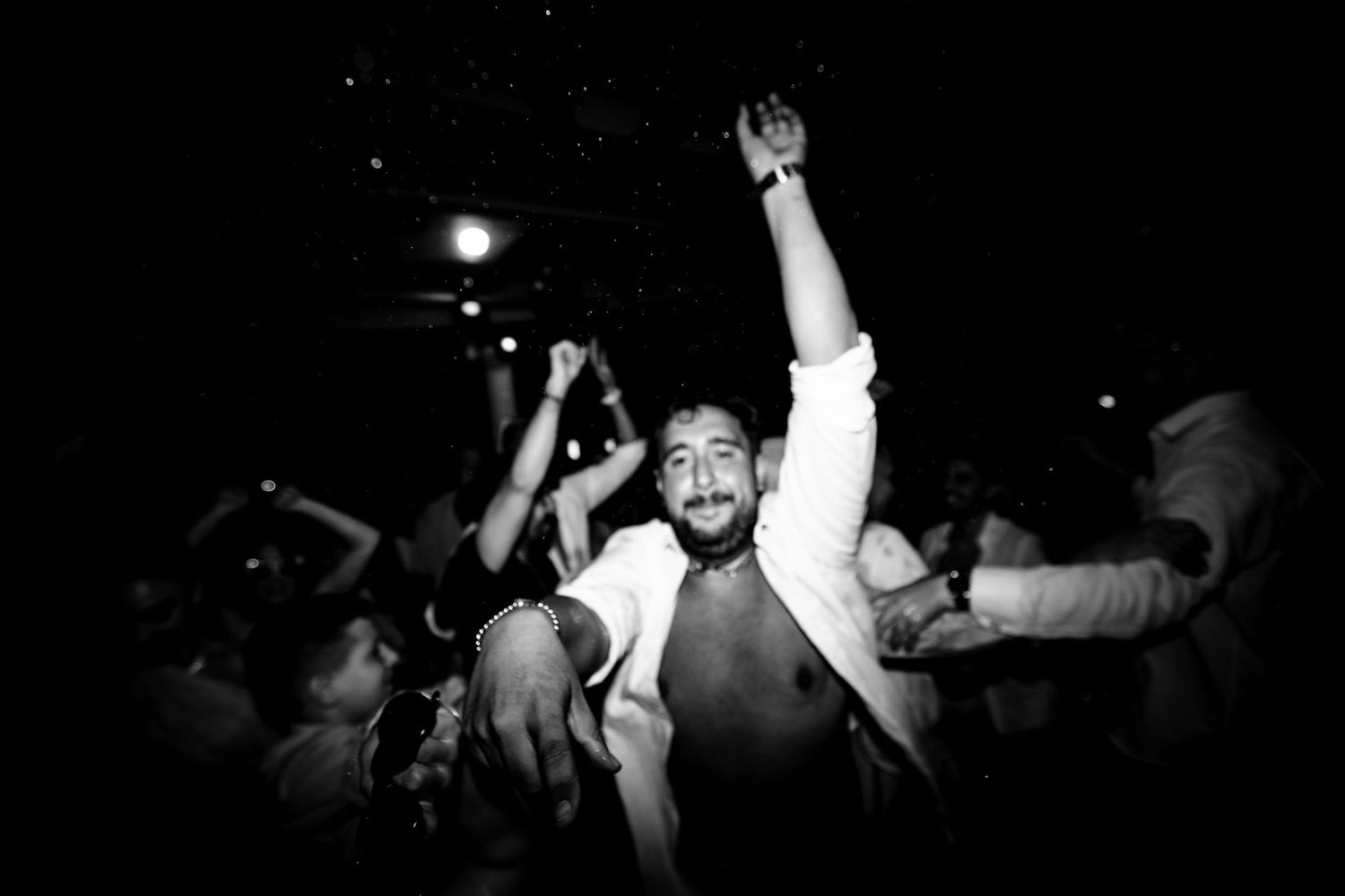 People dancing with raised arms in a dark party environment.