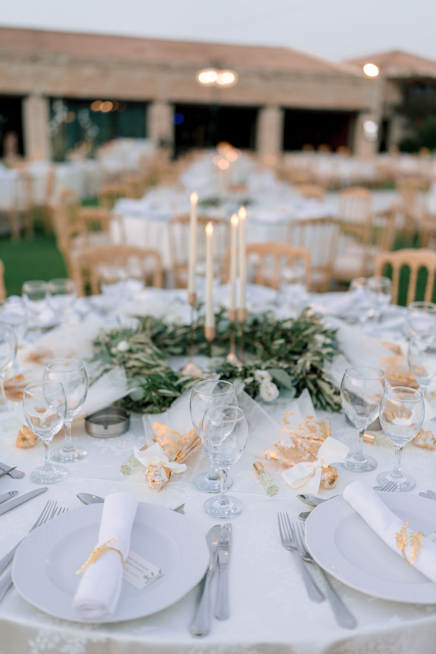 Elegant wedding reception tables set with white linens, glassware and greenery centerpieces.