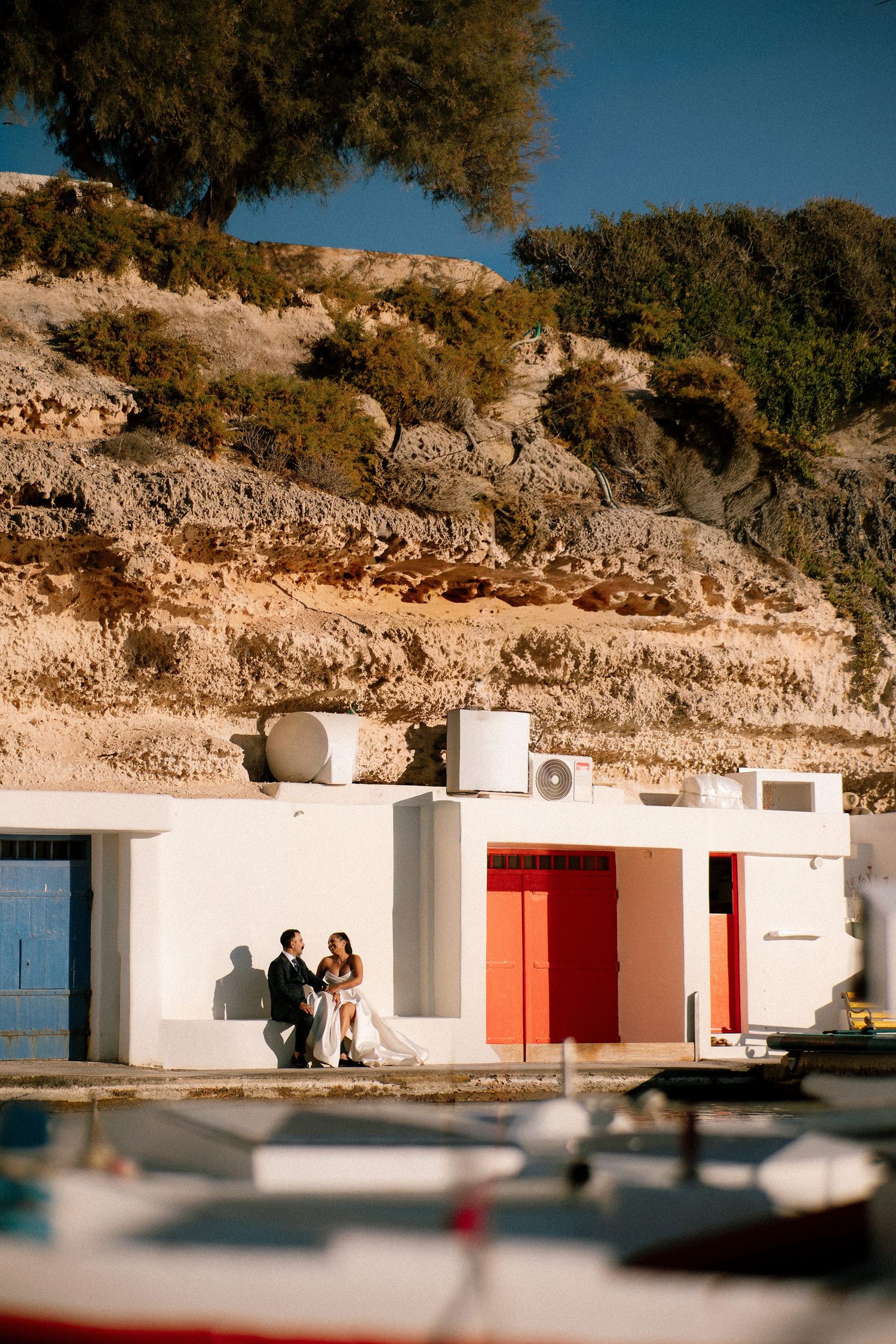Traditional white Mediterranean buildings with red doors nestled against rocky cliffs by the sea.