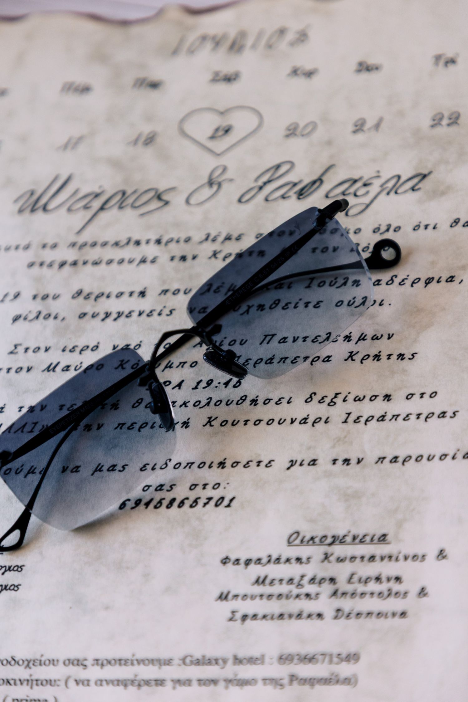 Stylish sunglasses on handwritten wedding invitation with Greek text.
