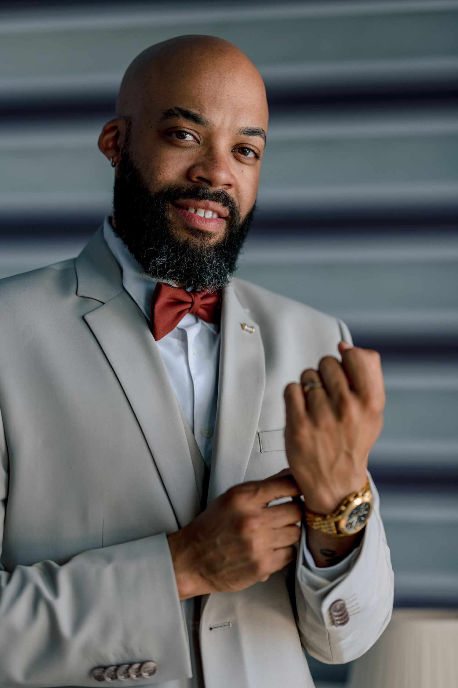 Person wearing a light grey suit with red bow tie adjusts cufflinks.