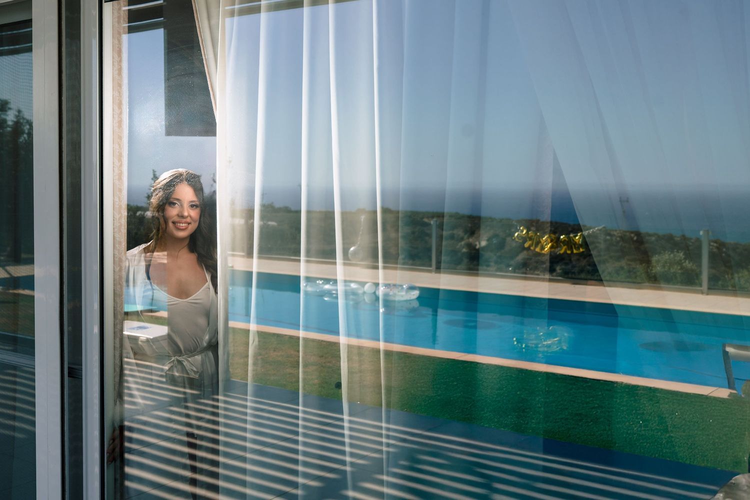 Reflection in window shows oceanfront pool view during wedding morning preparations.