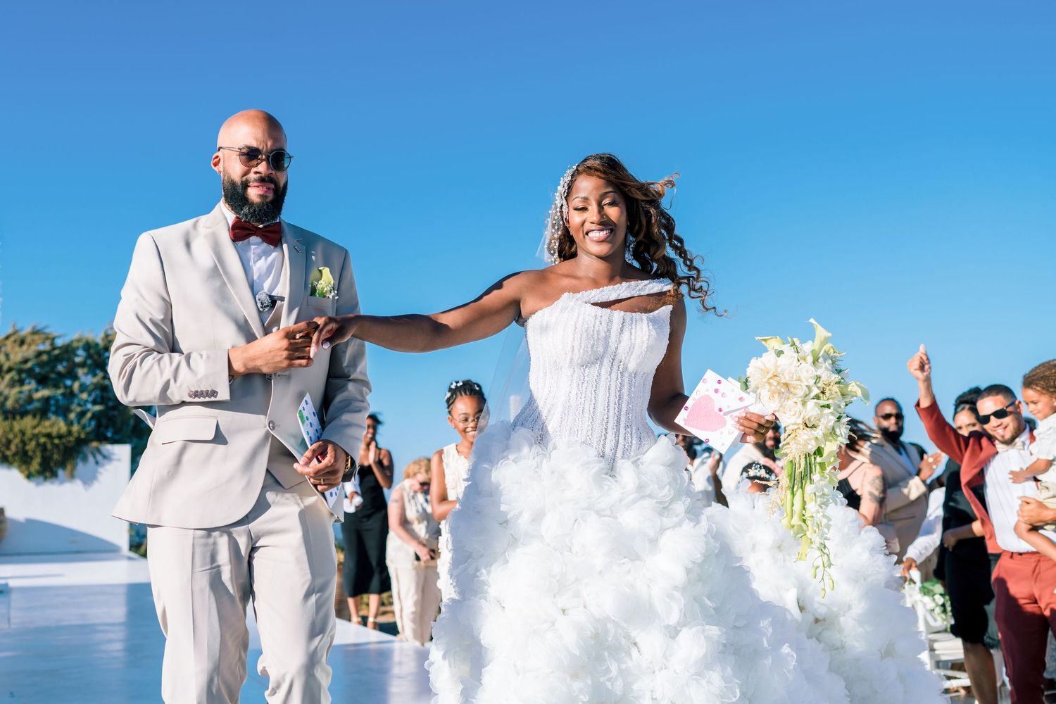 Wedding celebration on a bright sunny day with guests in white and beige attire.