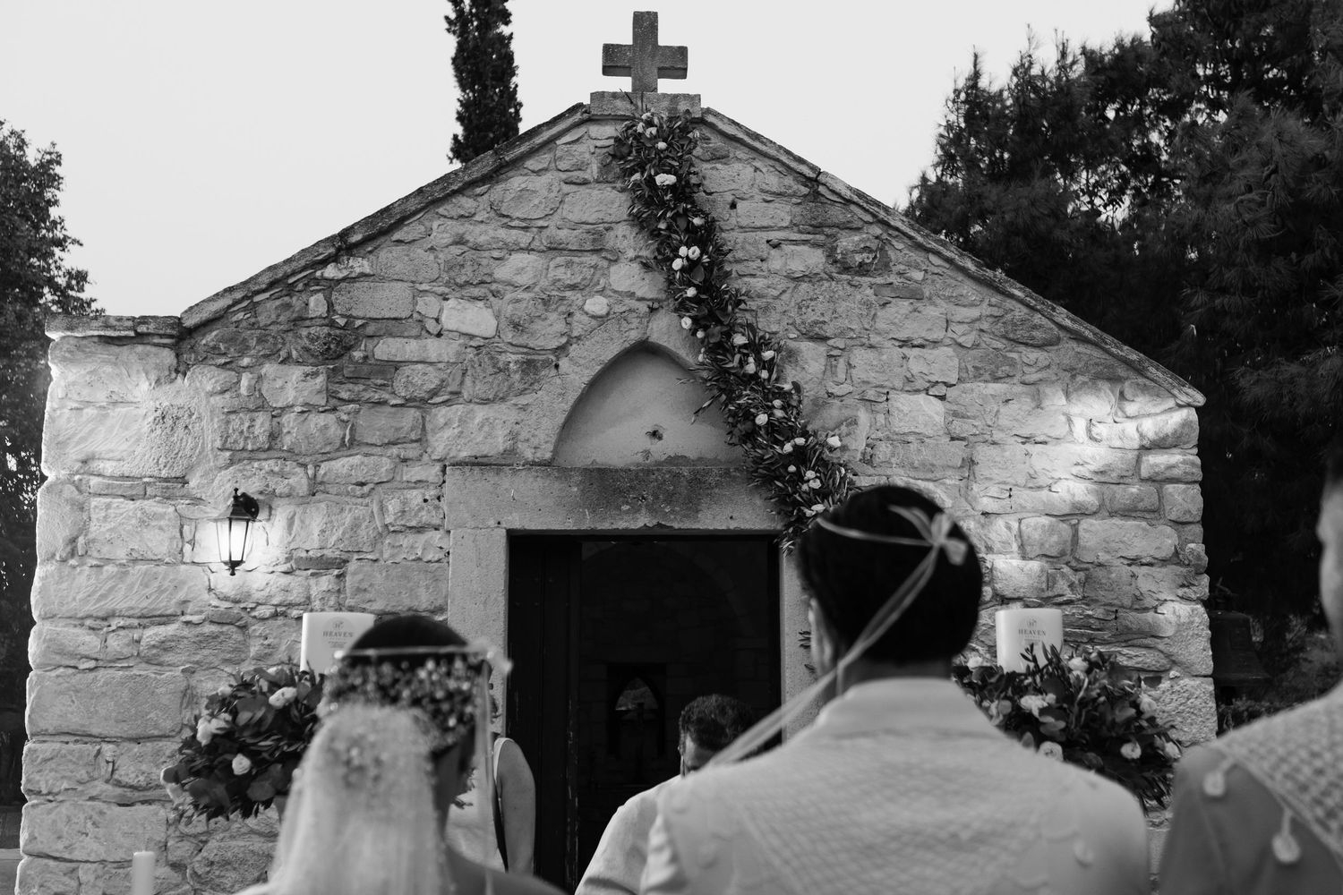 Stone chapel with cross on top photographed in black and white against cloudy sky.